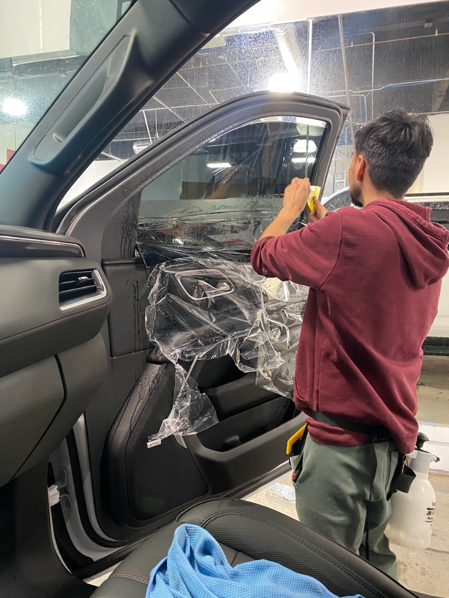 Person applying window tint to a car door inside a shop.