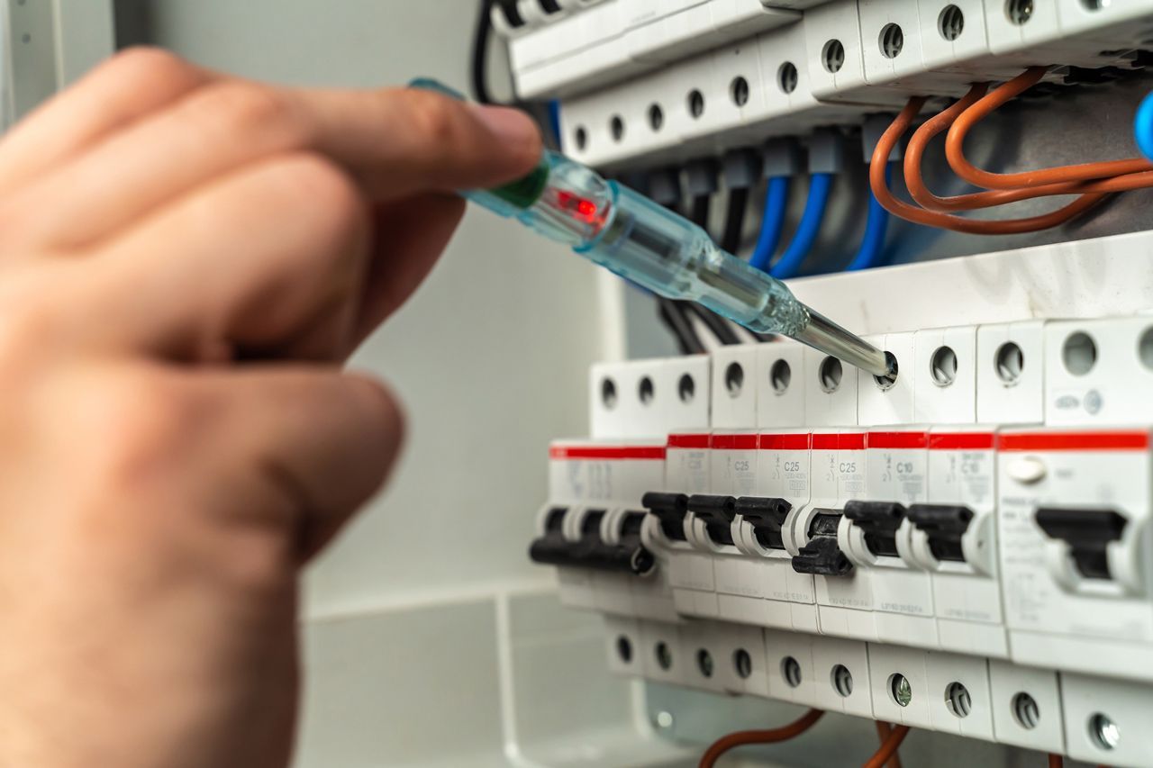 A person is working on an electrical box with a screwdriver.