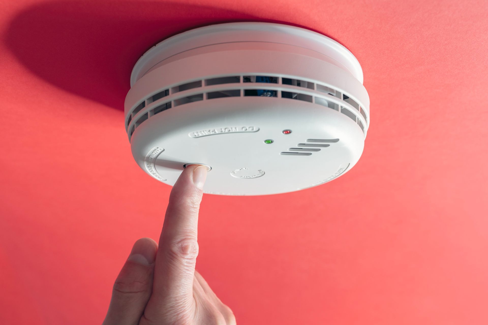 A person is pressing a button on a smoke detector.