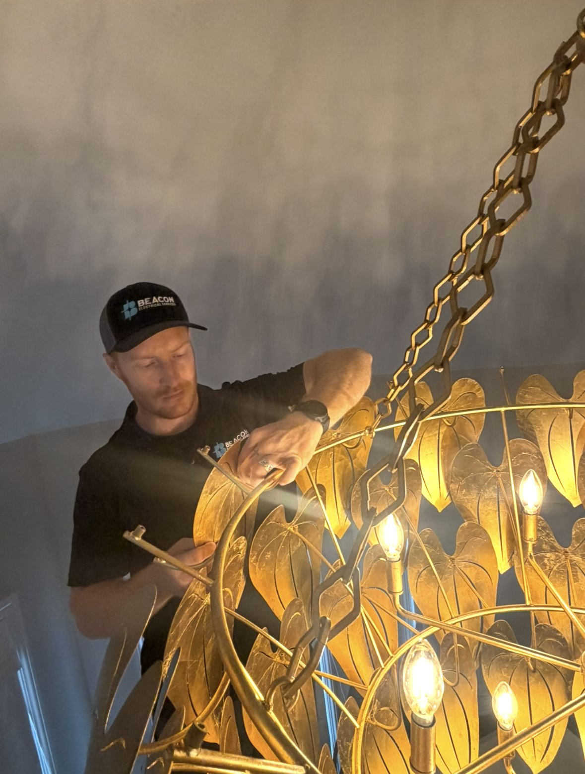 Person adjusting a glowing chain chandelier in a dim room