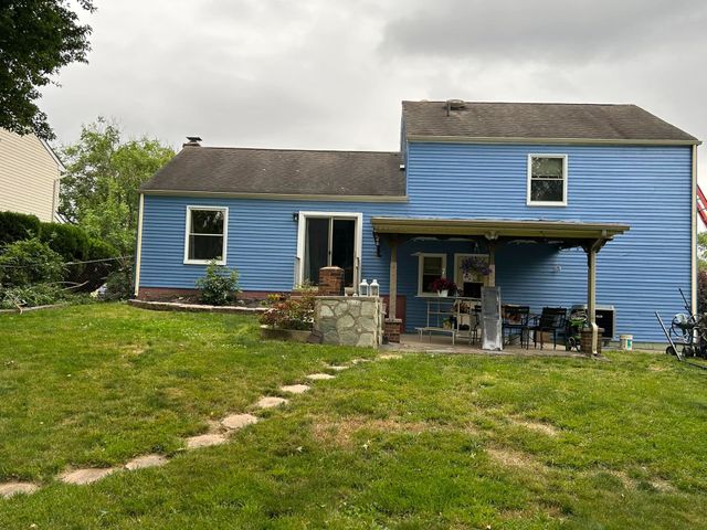 The back of a blue house with a large lawn in front of it.