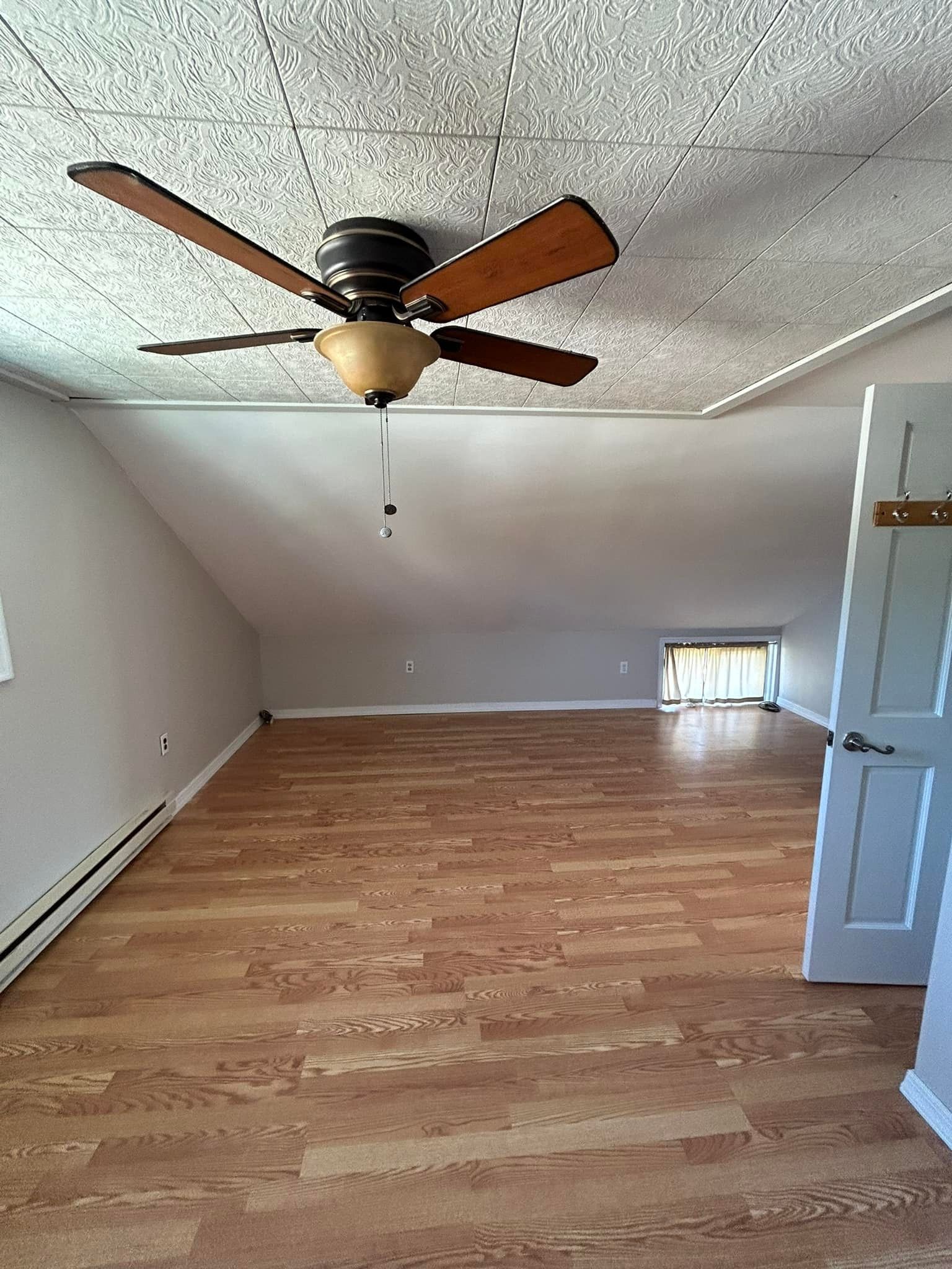 An empty room with hardwood floors and a ceiling fan.