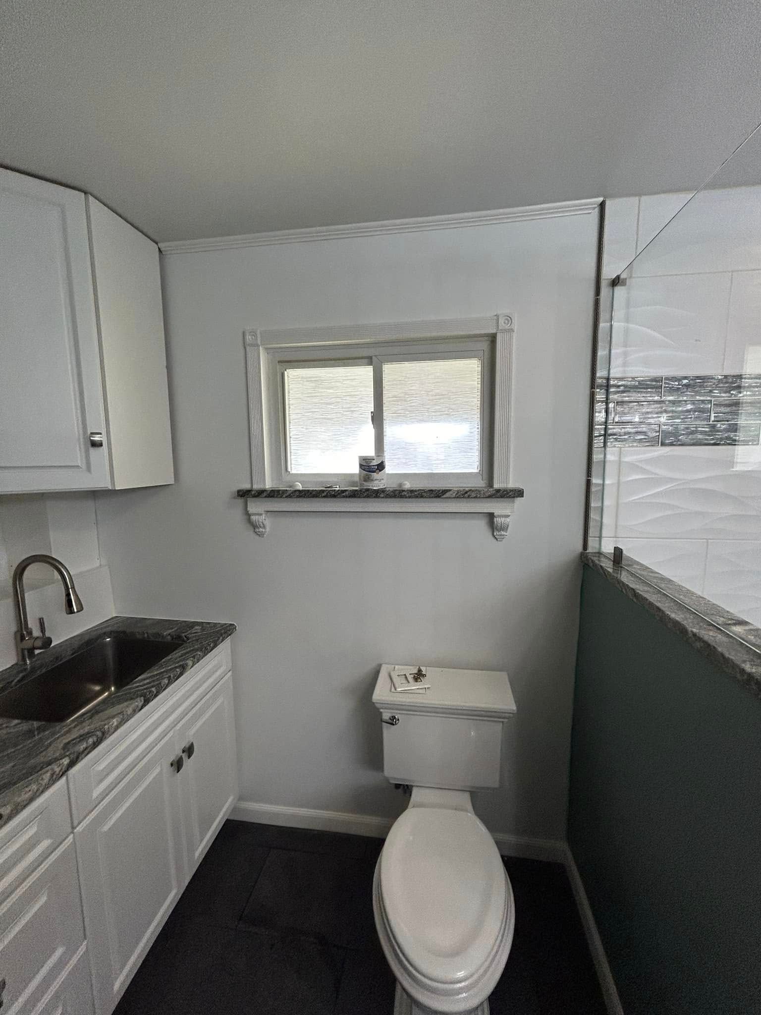 A bathroom with a toilet , sink and window.
