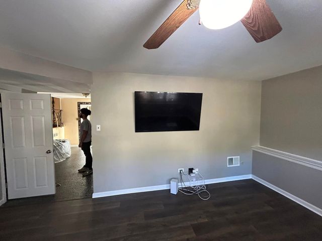 A living room with a flat screen tv mounted on the wall and a ceiling fan.
