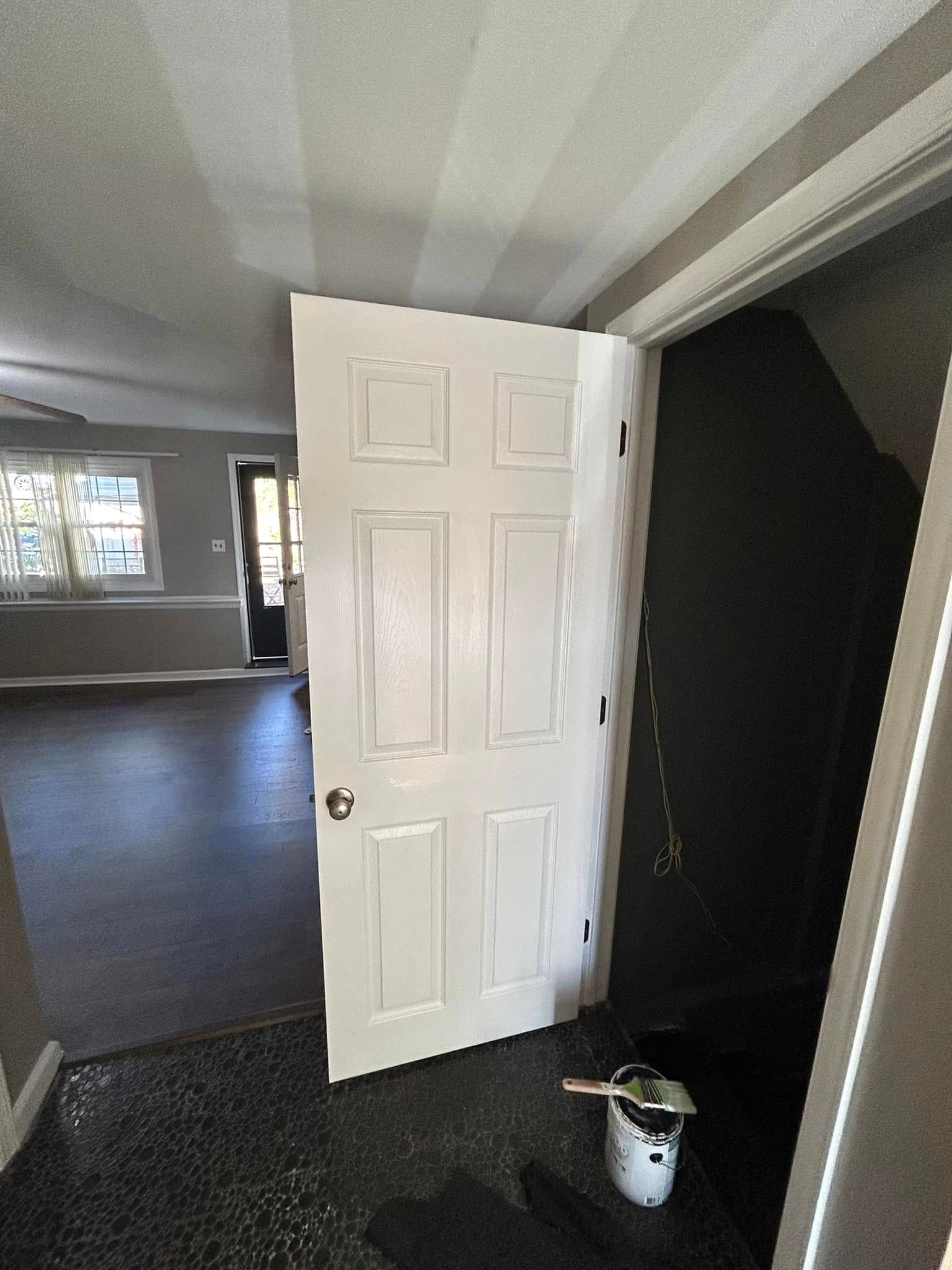 A white door is open to a room with a bucket of paint on the floor.