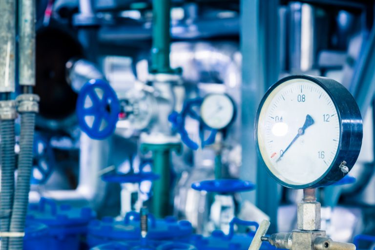 Pressure gauge in industrial setting with blue pipes and valves.