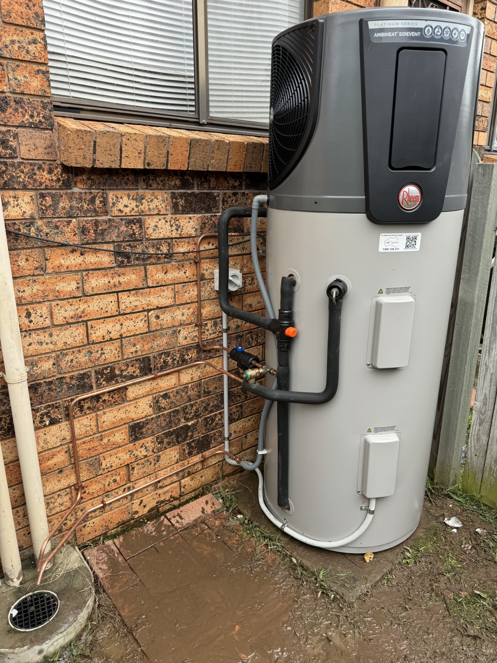 Gray and black heat pump water heater next to a brick wall.