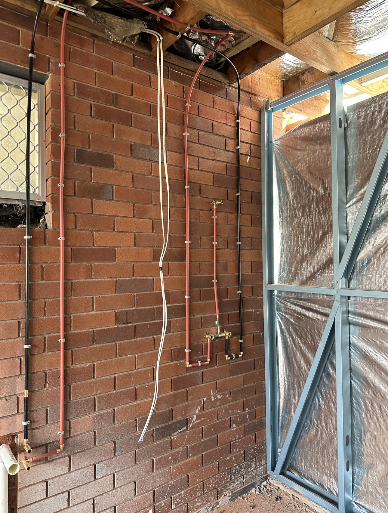 Brick wall with pipes and wiring. A metal frame with reflective insulation is on the right side.