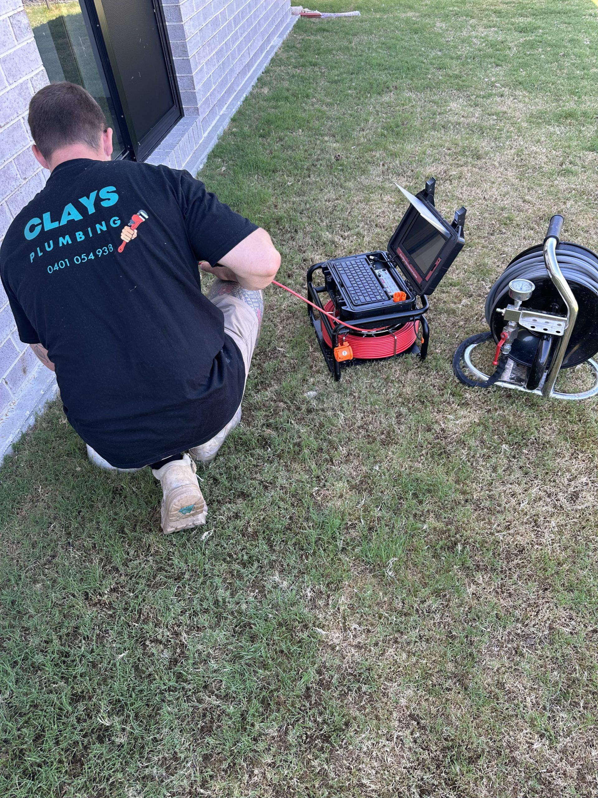 Plumber in black shirt working with sewer inspection equipment on a grassy lawn.