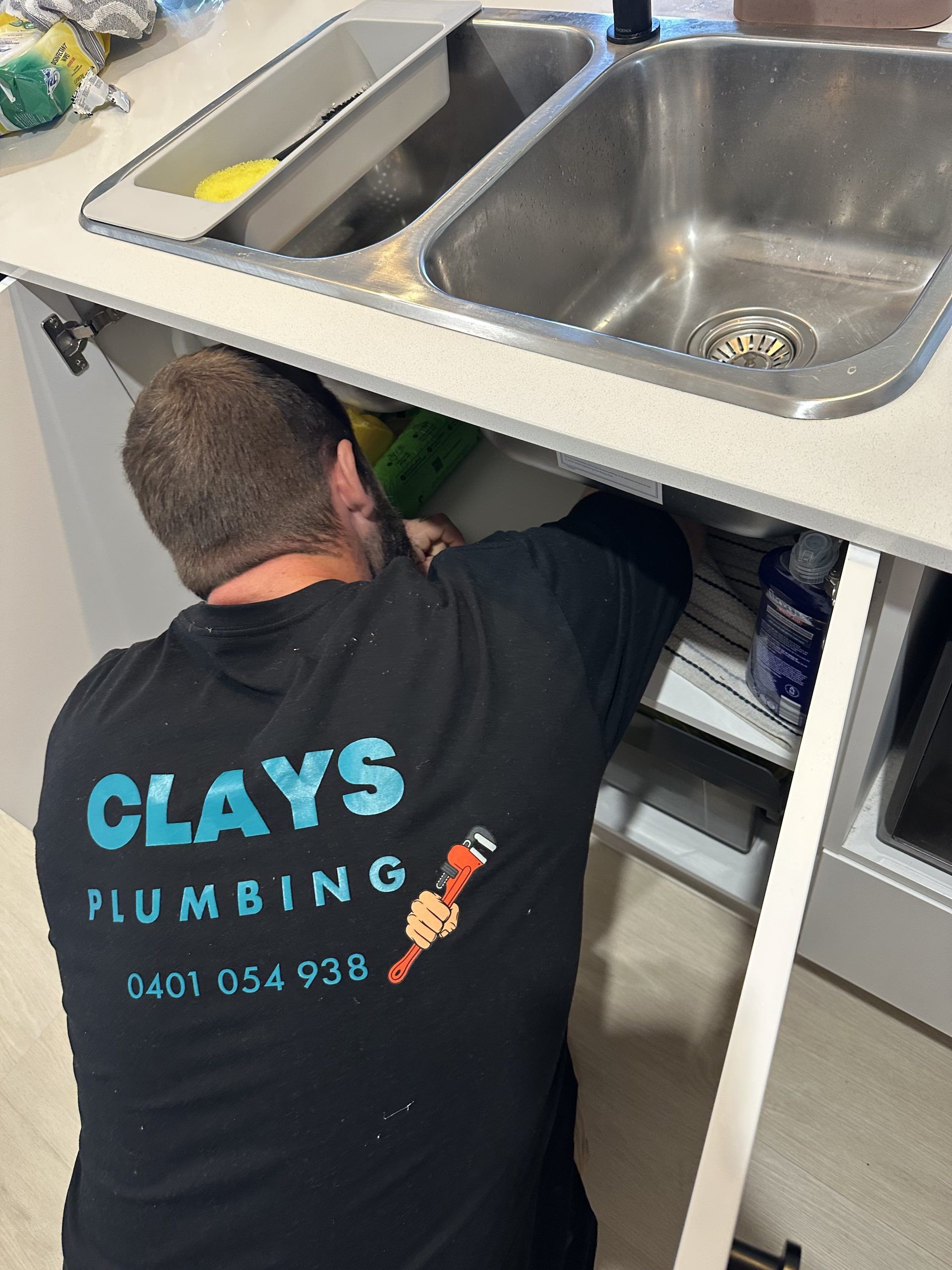 Plumber working under a kitchen sink. Wearing a black shirt with 