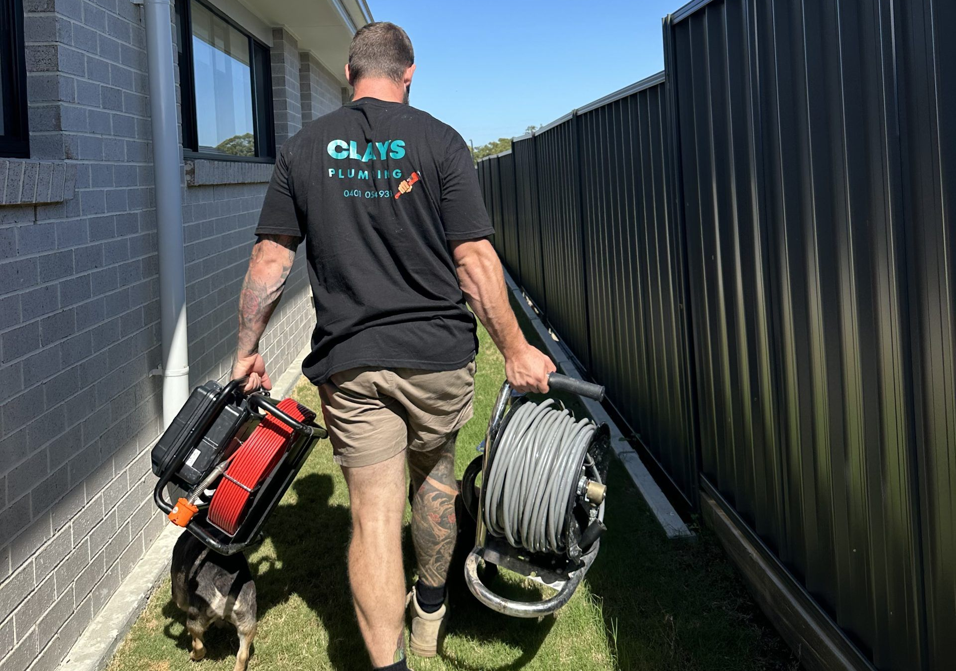 Man carrying equipment and a dog walking along a fence.