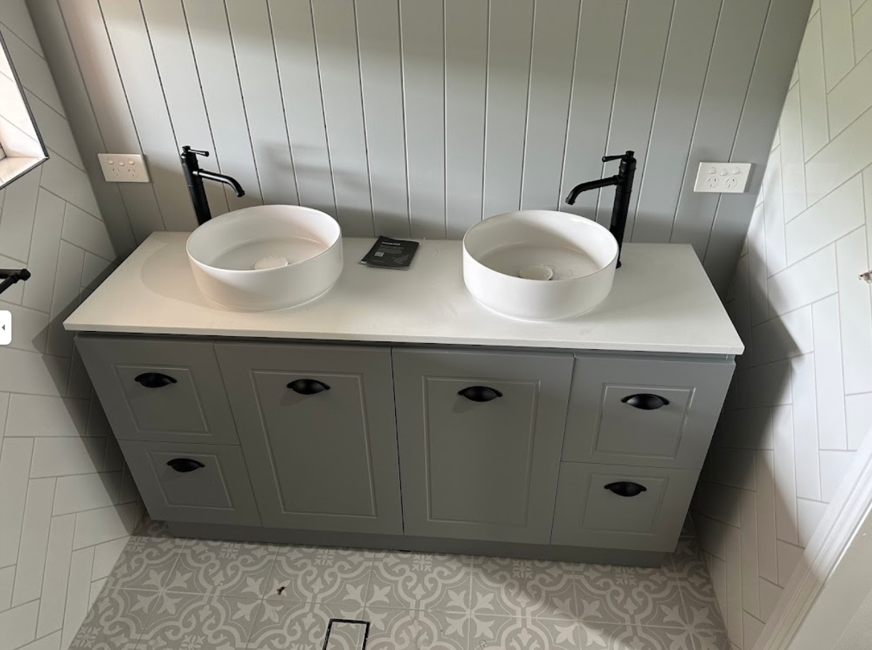 Bathroom vanity with two white bowl sinks, gray cabinet, black faucets, and gray and white patterned floor tiles.