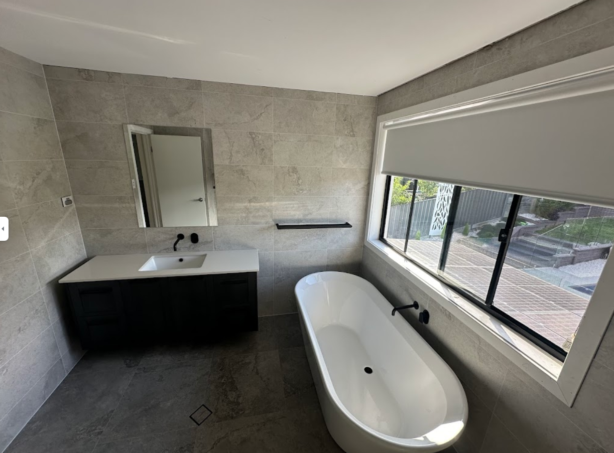 Modern bathroom with gray tiled walls, black vanity, white tub, and large window.