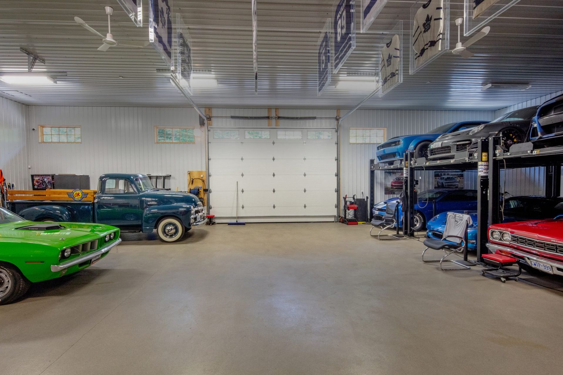 Spacious garage with classic cars, blue car lift, red tool cabinets, and a large white roll-up door