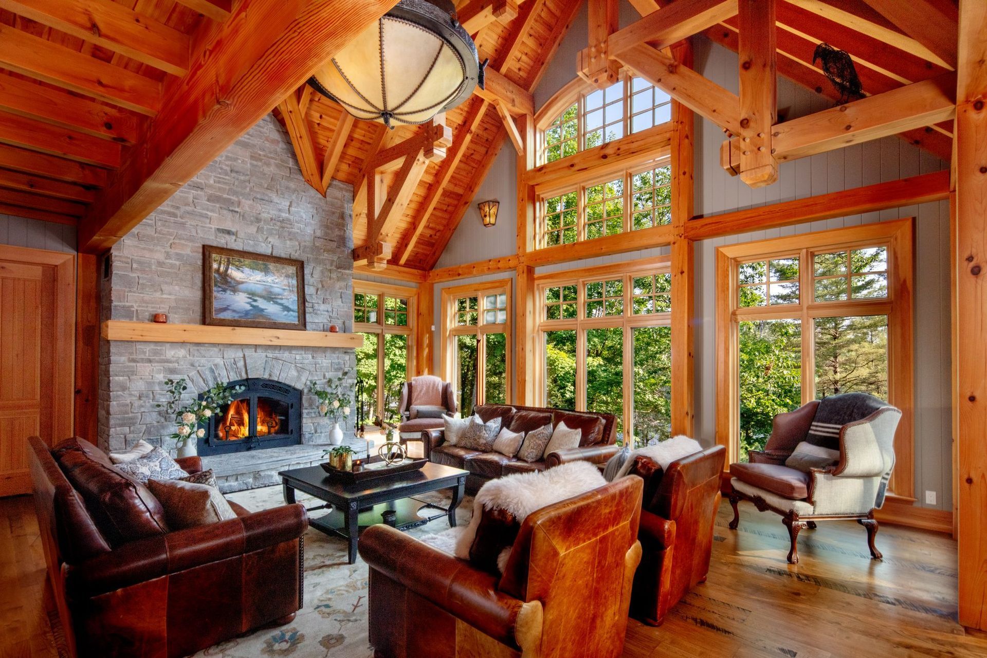 Cozy timber-framed living room with stone fireplace, leather chairs, and large sunlit windows