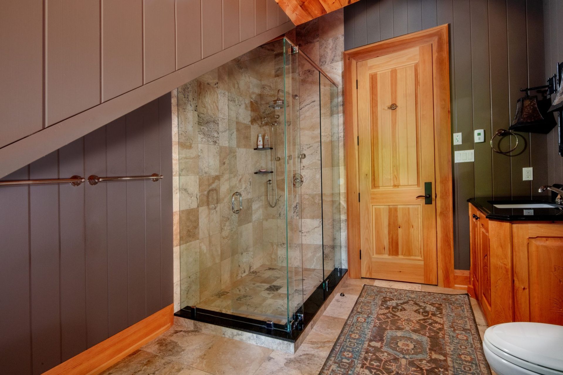 Staircase with a stone-faced glass shower enclosure beside a wooden door in a bathroom.