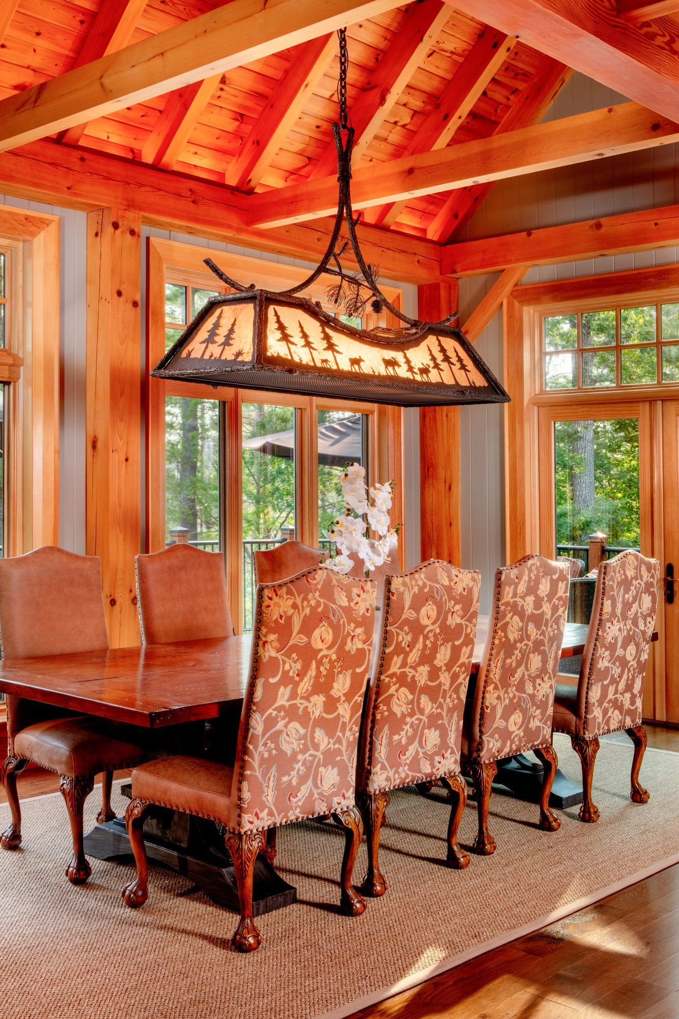 Elegant dining room with carved chairs, wooden table, and large pendant light in a cozy cabin setting