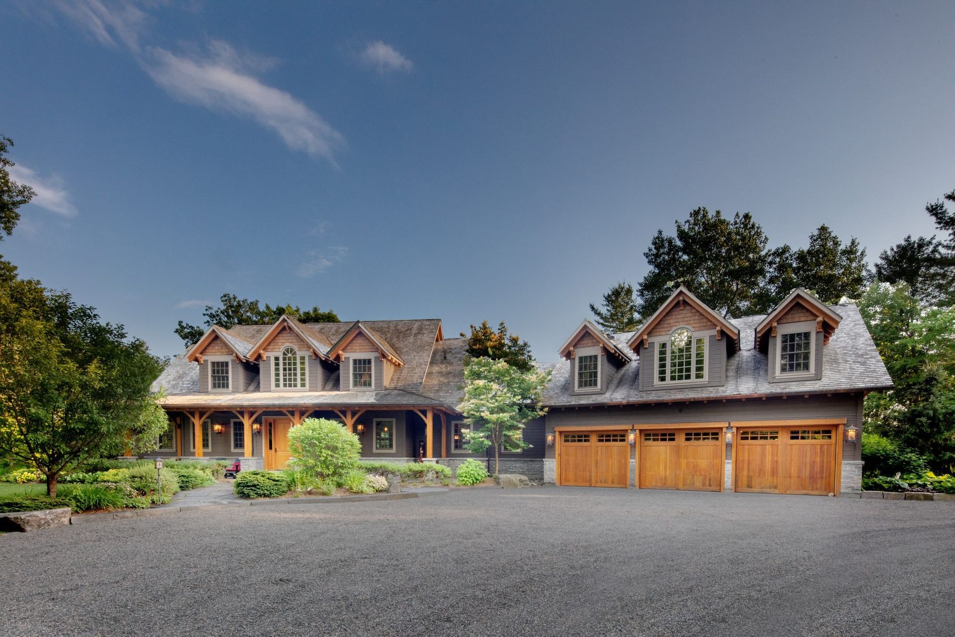 Two large modern houses with stone facades and garages, set beside a wide gravel driveway under a blue sky