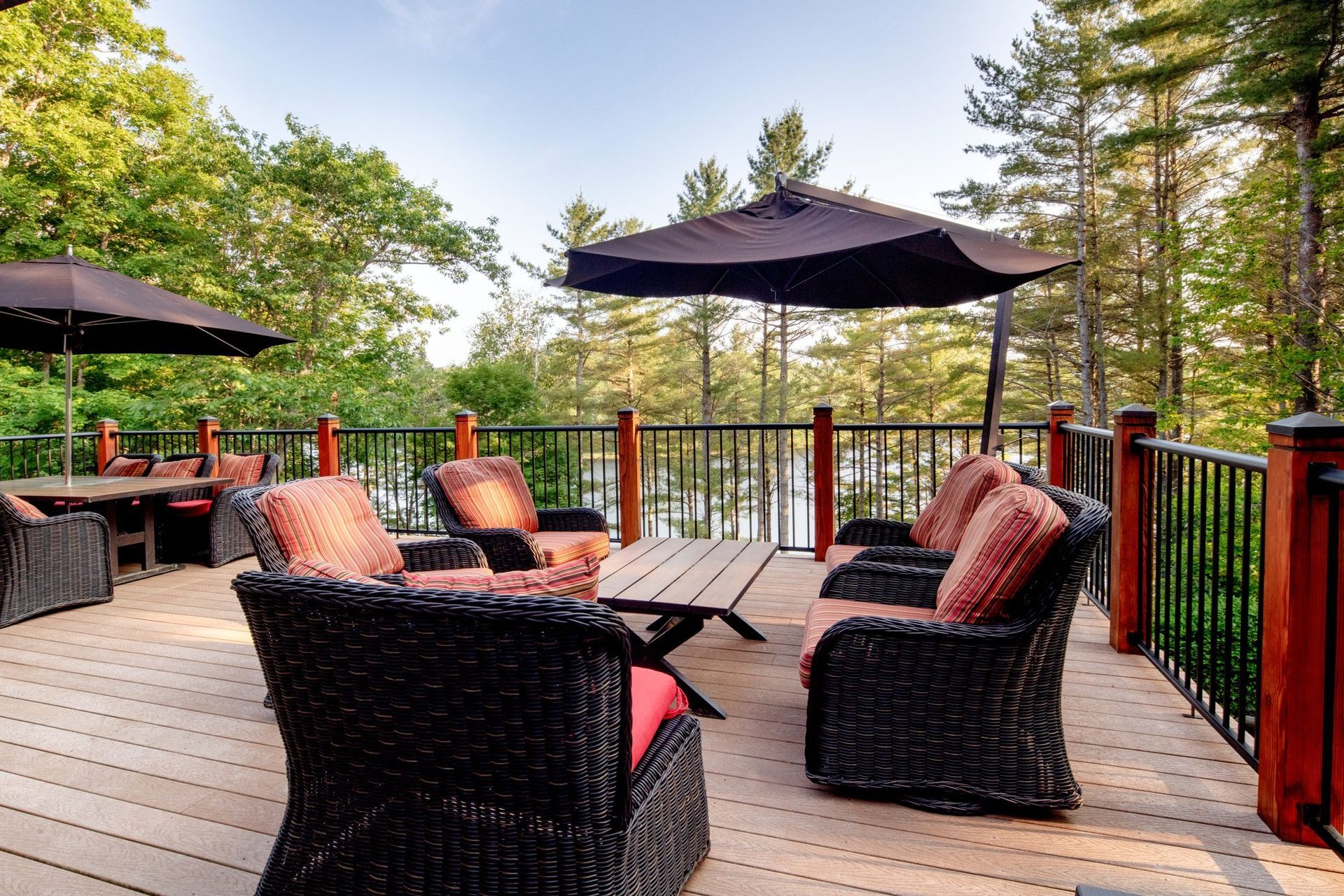 Outdoor deck with wicker chairs, red cushions, and black umbrellas overlooking trees