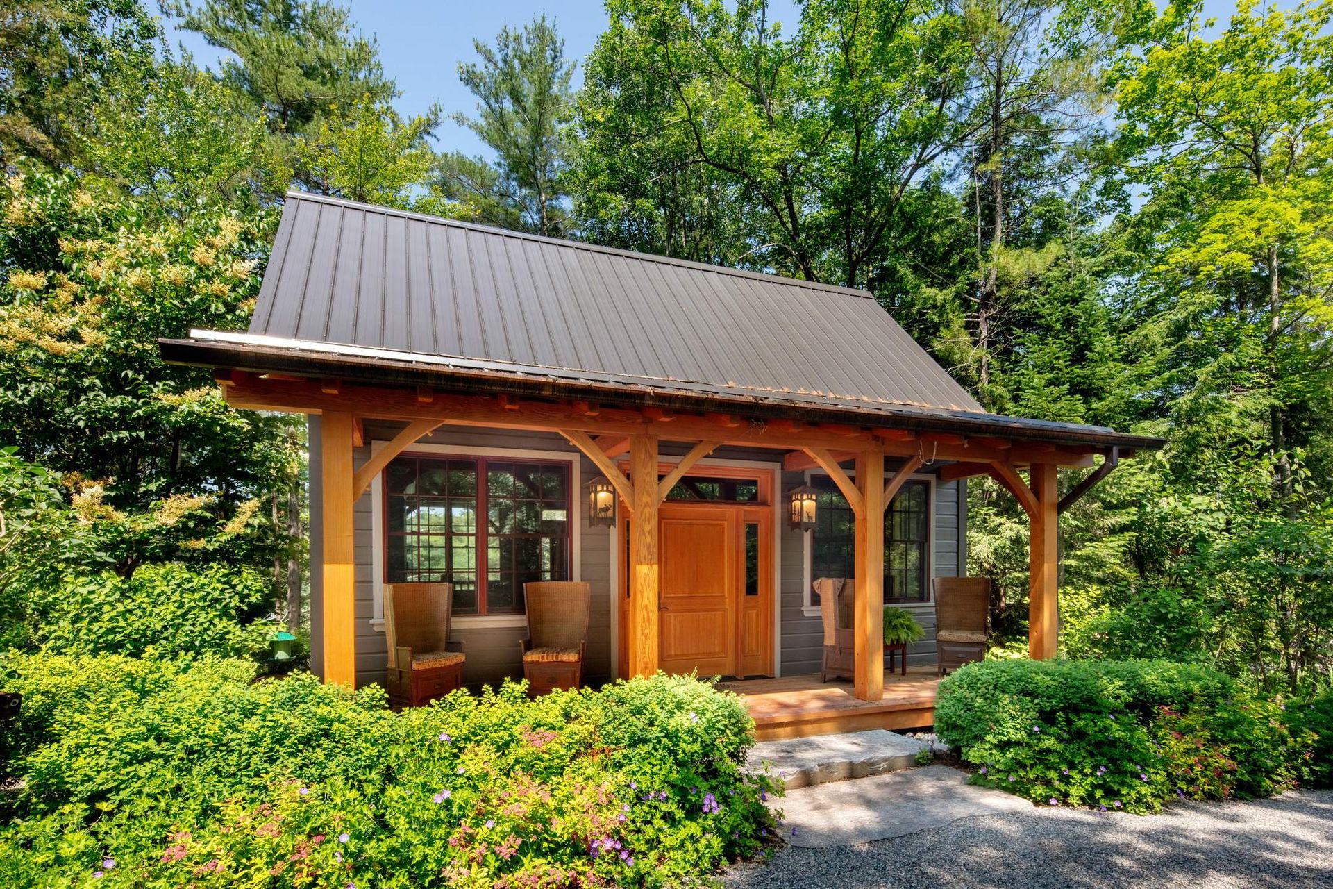 Small wooden cabin with a gray roof surrounded by lush green trees and shrubs