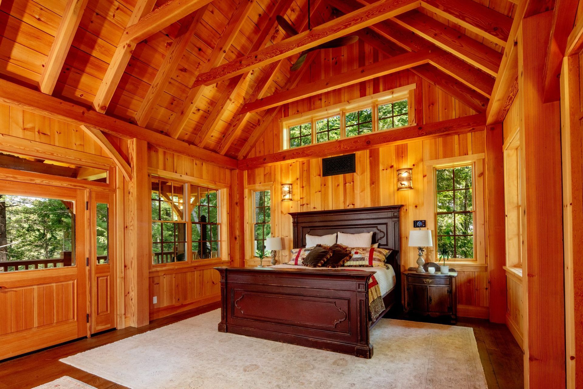 Cozy wood-paneled bedroom with a large bed, vaulted ceiling, and windows overlooking trees