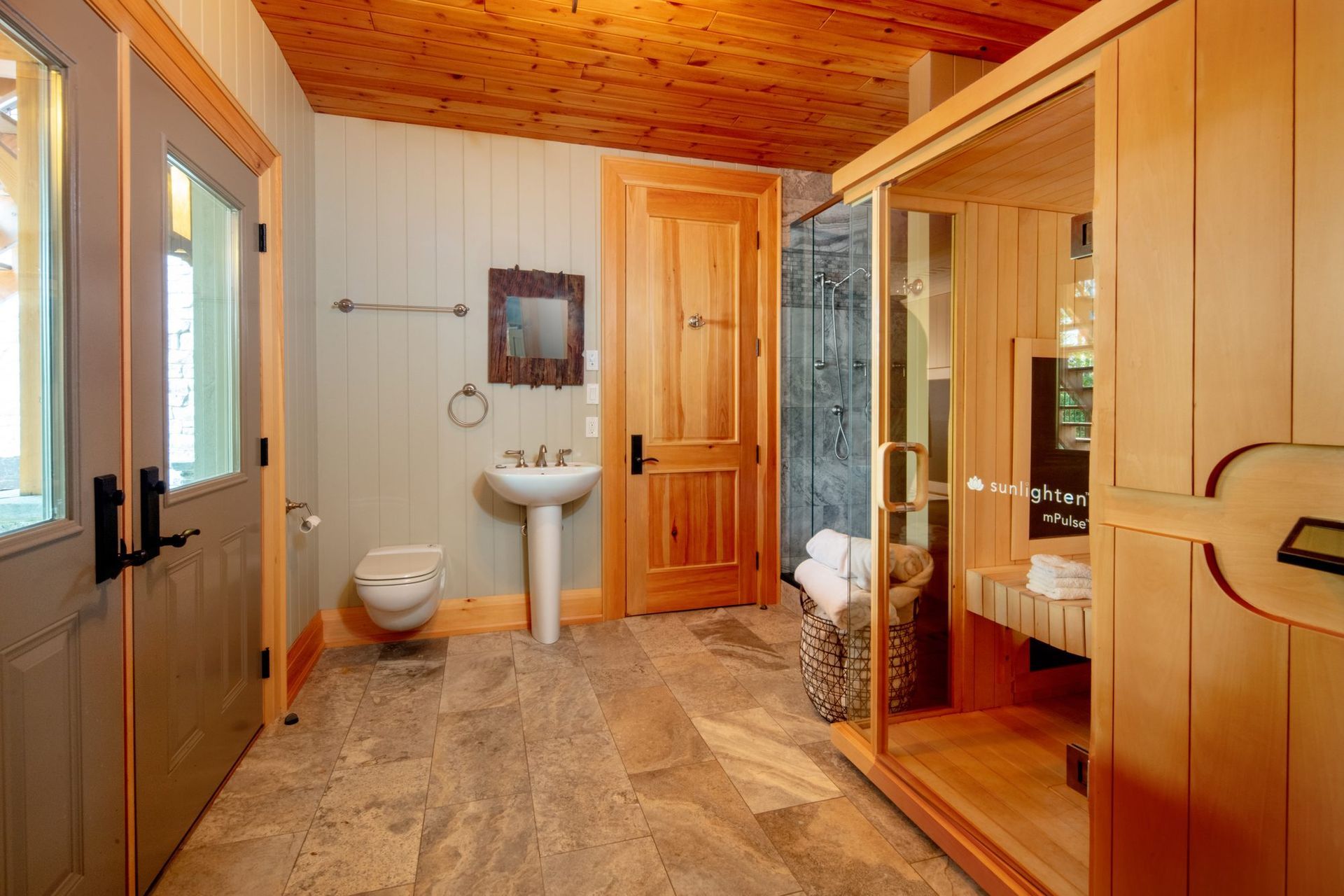 Spacious bathroom with wood-paneled walls, sink, toilet, shower, and a glass sauna or steam room.