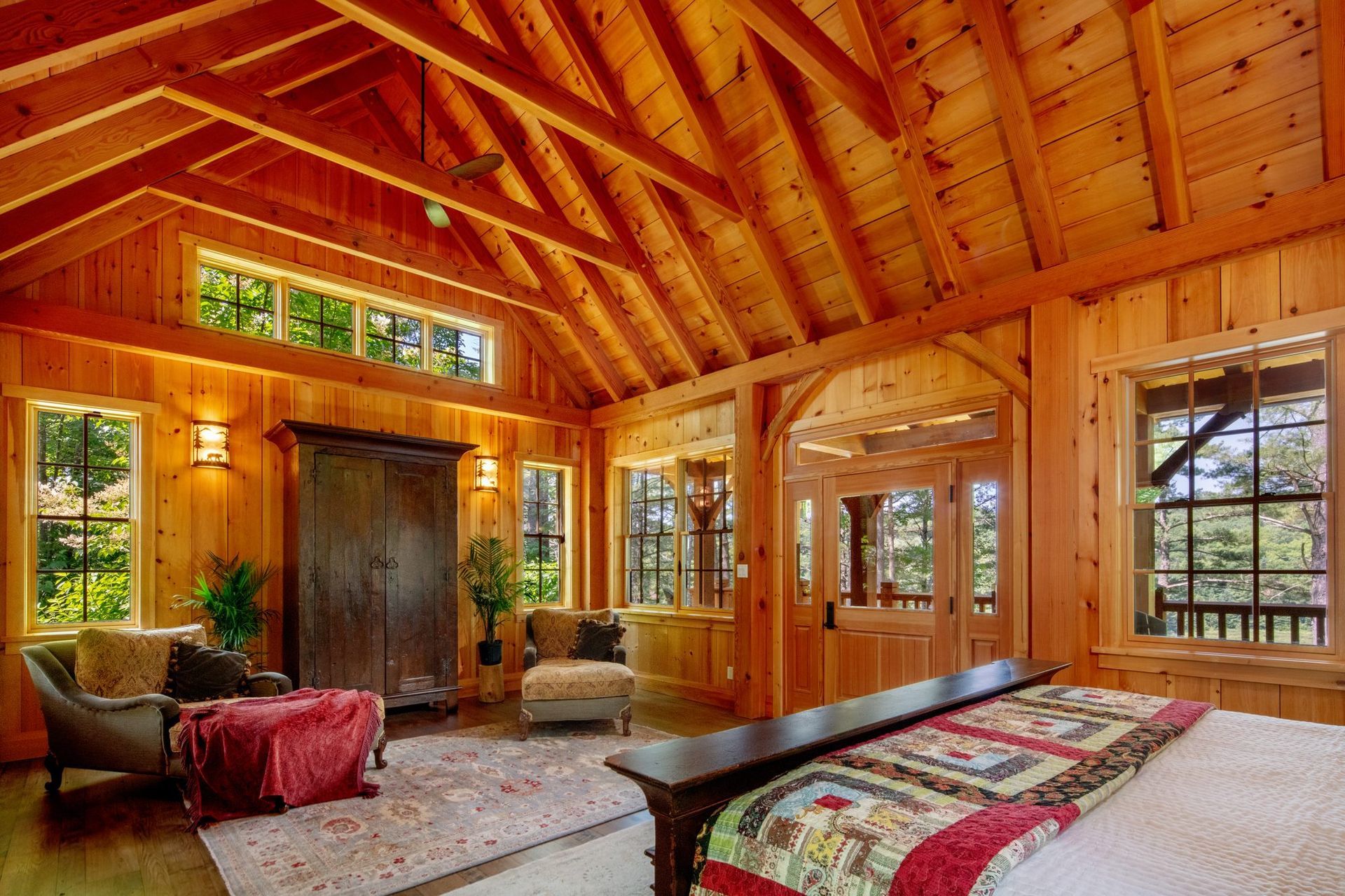 Cozy log cabin bedroom with wood beams, large windows, and a bed with colorful quilt