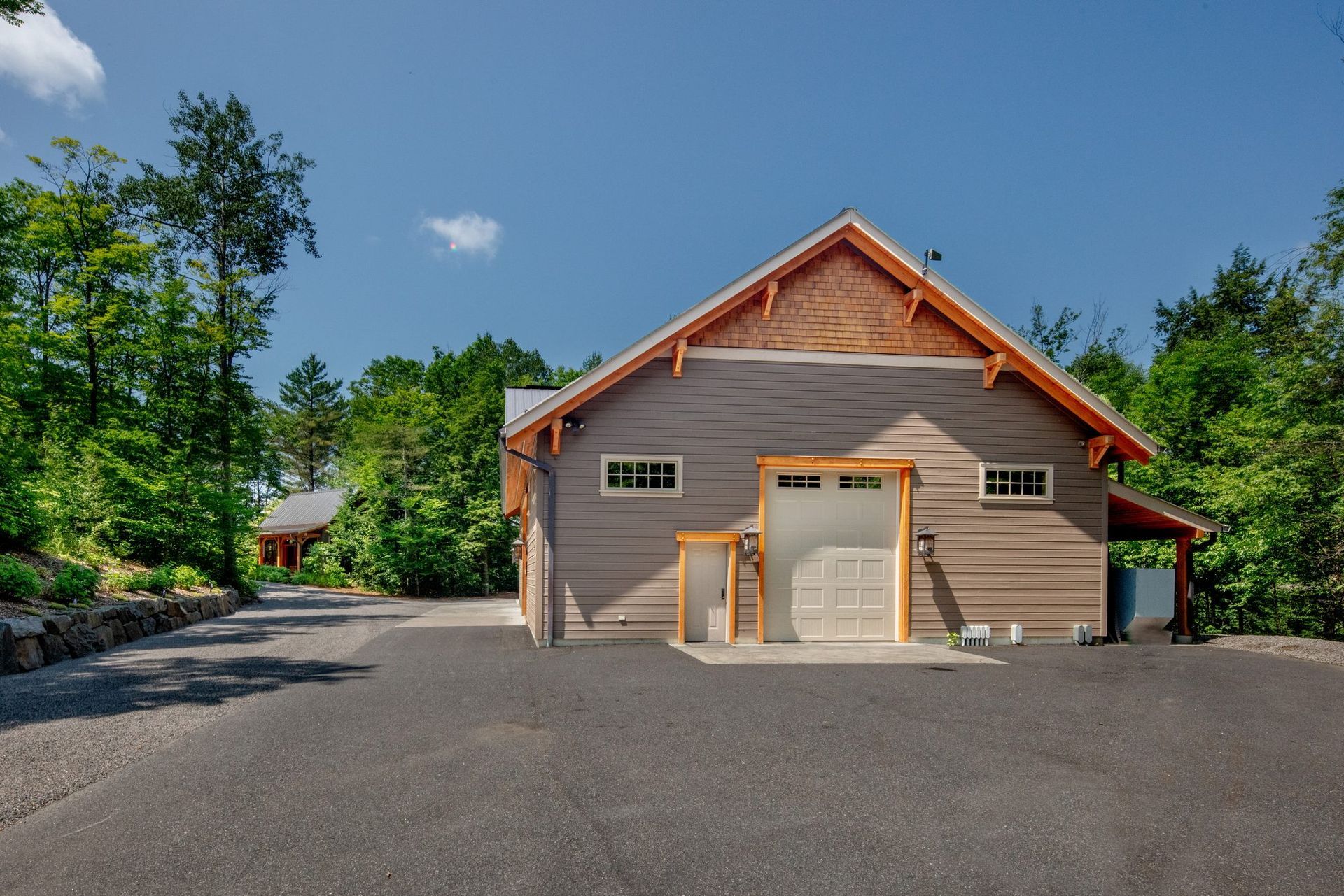 Small gray building with orange trim and a gravel driveway, surrounded by trees under a blue sky