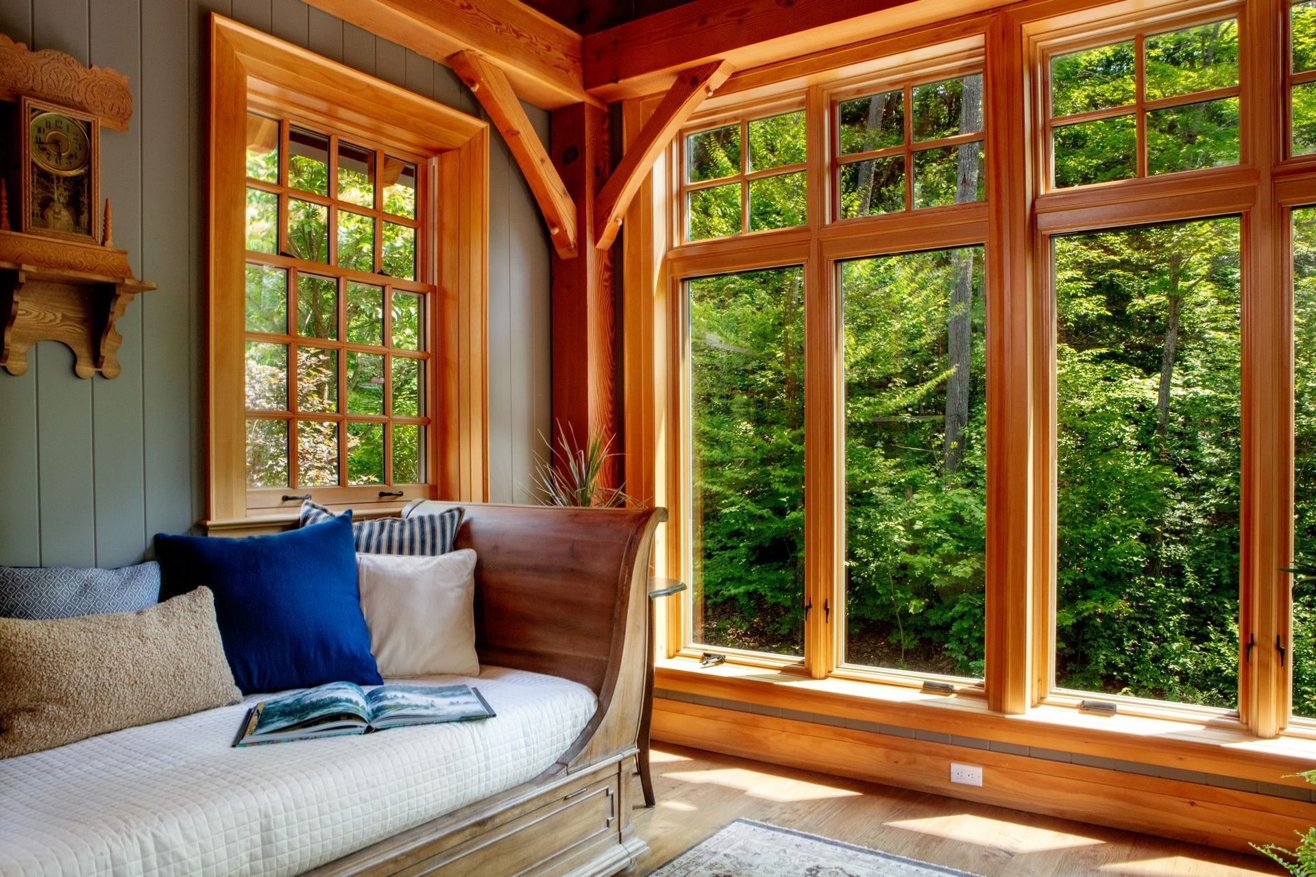 Cozy sunlit room with a white couch and large wooden-framed windows overlooking greenery