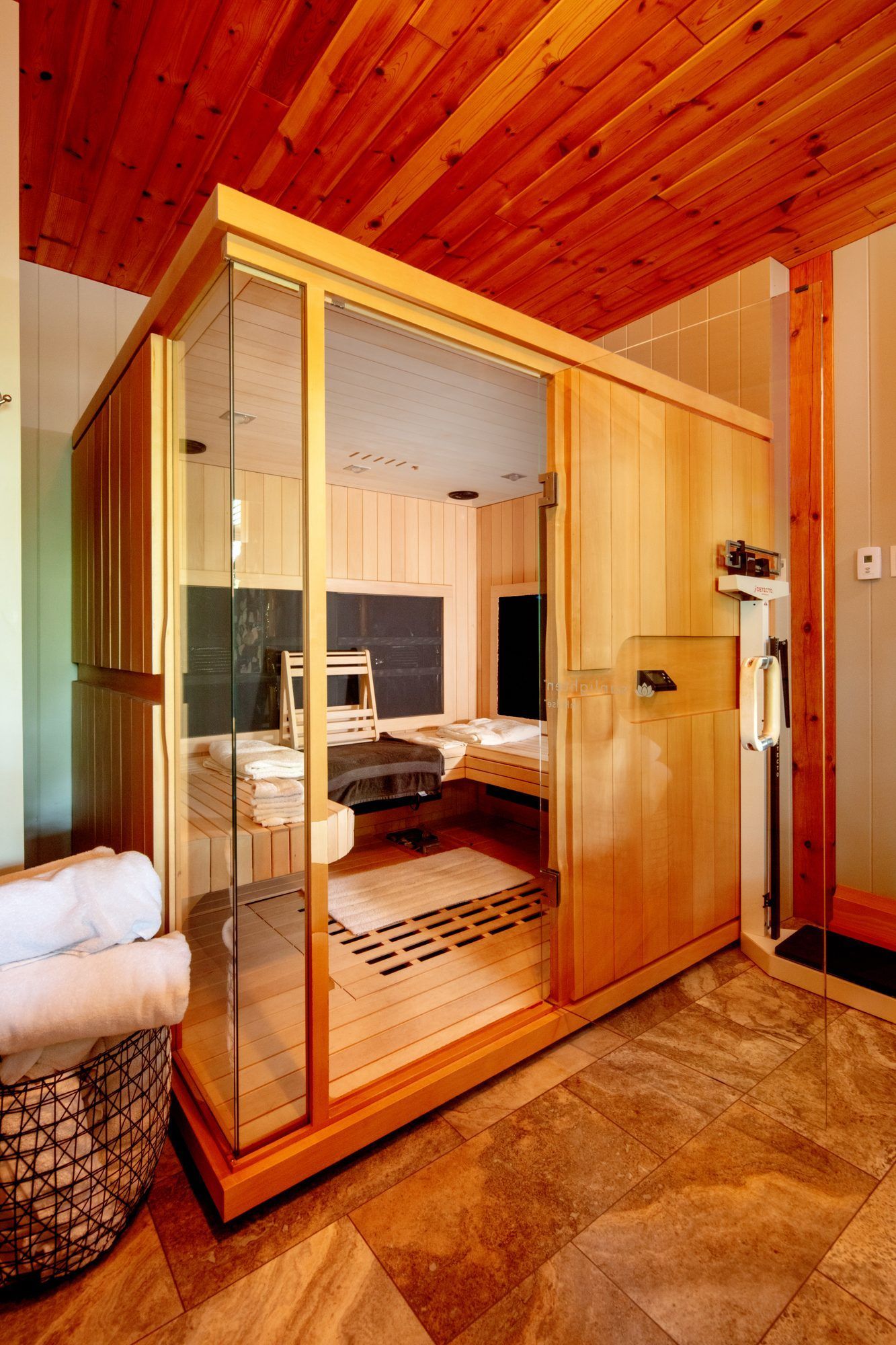 Wood-framed glass steam shower with wooden ceiling and stone tile floor in a spa-like bathroom