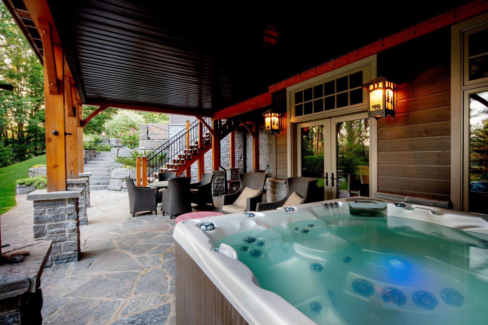 Covered patio with a hot tub, stone fireplace, seating area, and warm lantern lighting