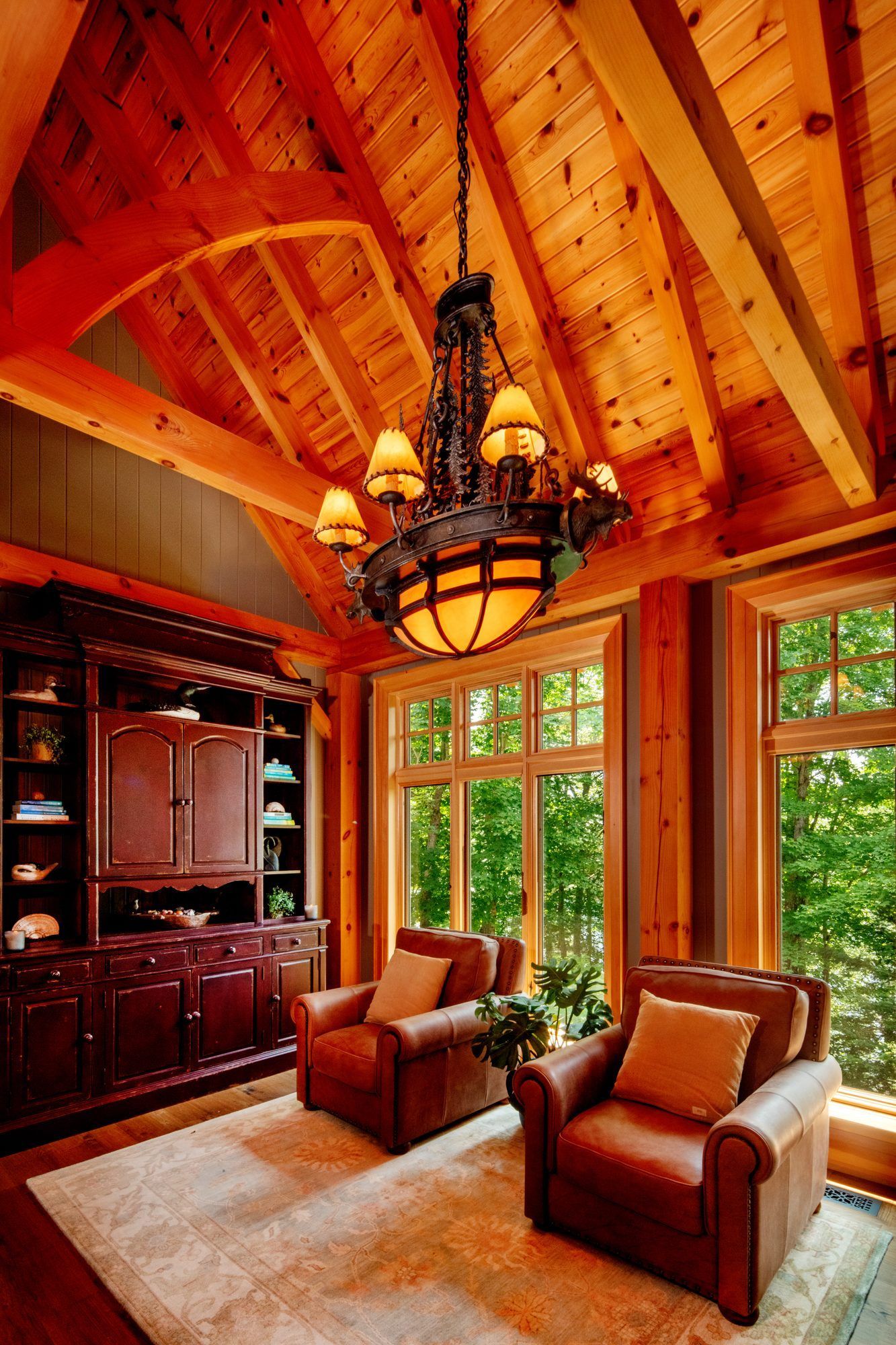 Cozy wood-paneled living room with vaulted ceiling, chandelier, large windows, and two leather chairs