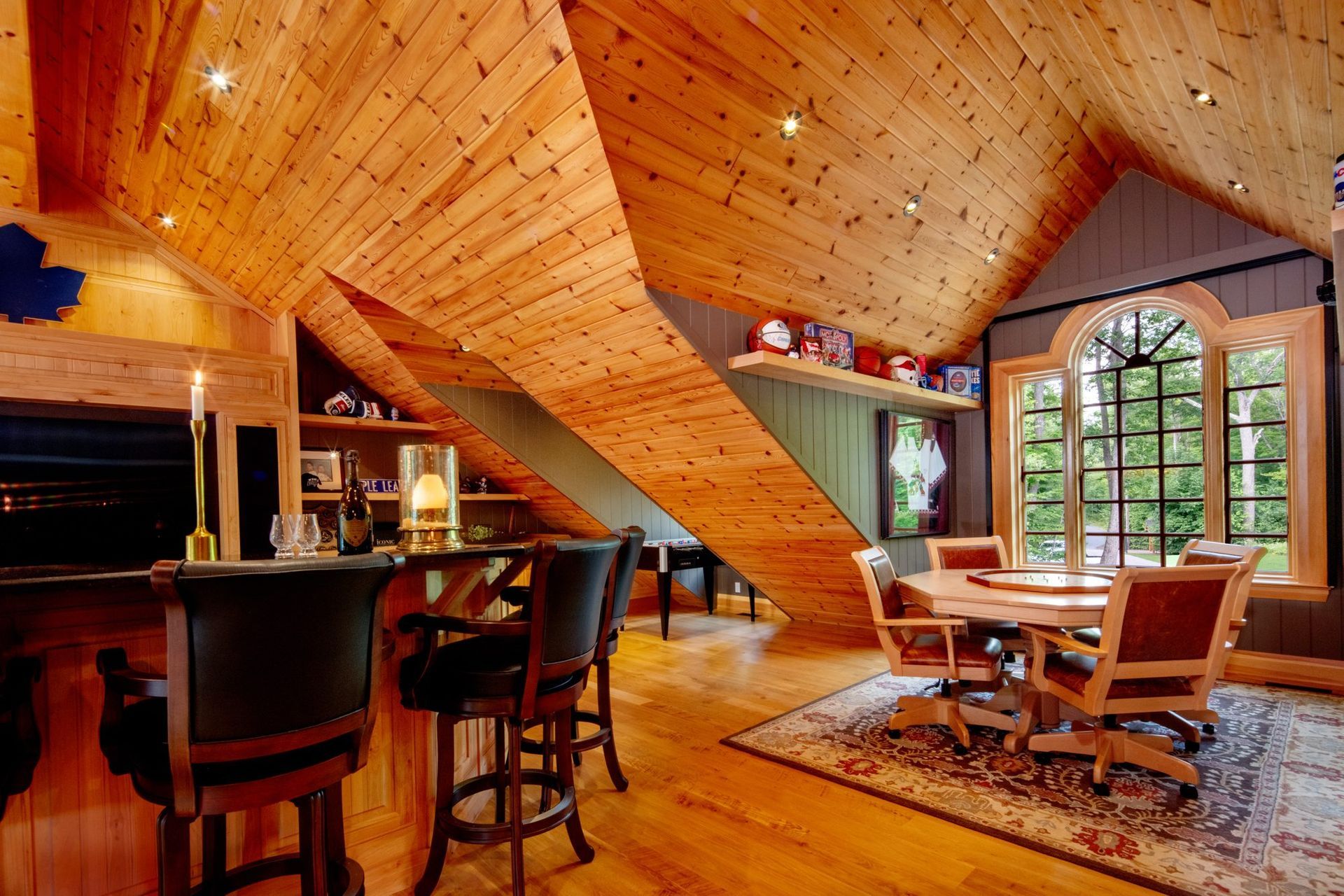 Warm wood-paneled loft with bar stools, cozy seating, and large windows overlooking the outdoors