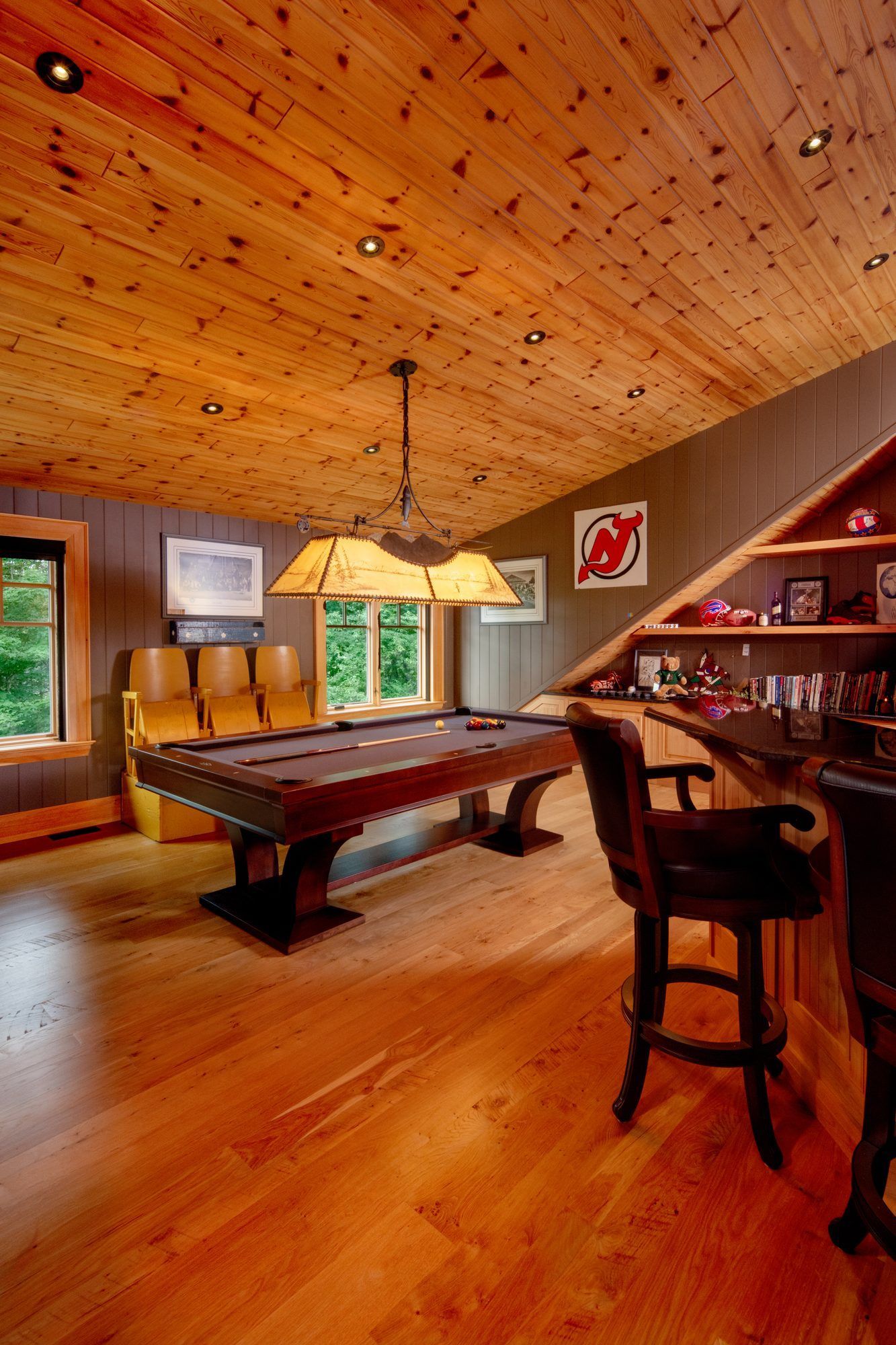 Wood-paneled game room with pool table, bar stools, and warm lighting