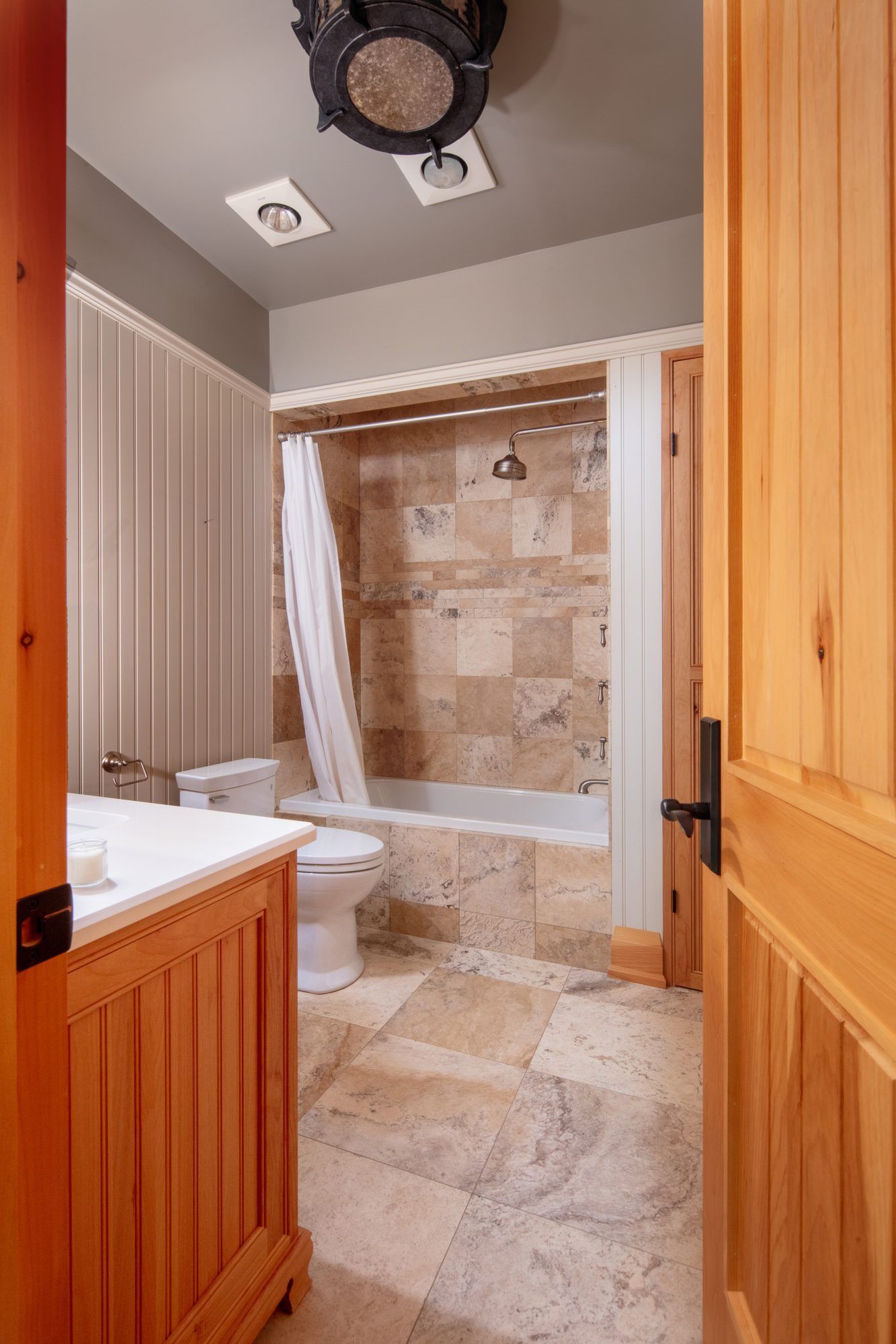 Bathroom with stone-tile shower, toilet, and wooden vanity viewed through an open door