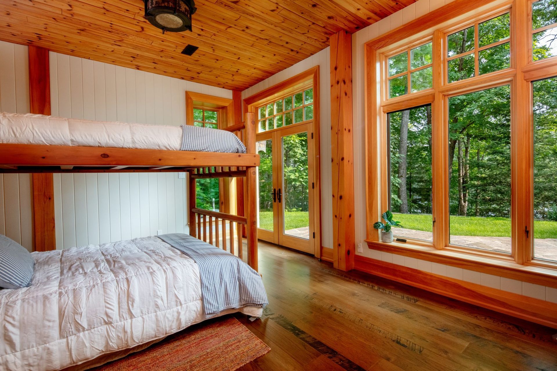 Wood-paneled cabin bedroom with bunk bed, large windows, and forest view