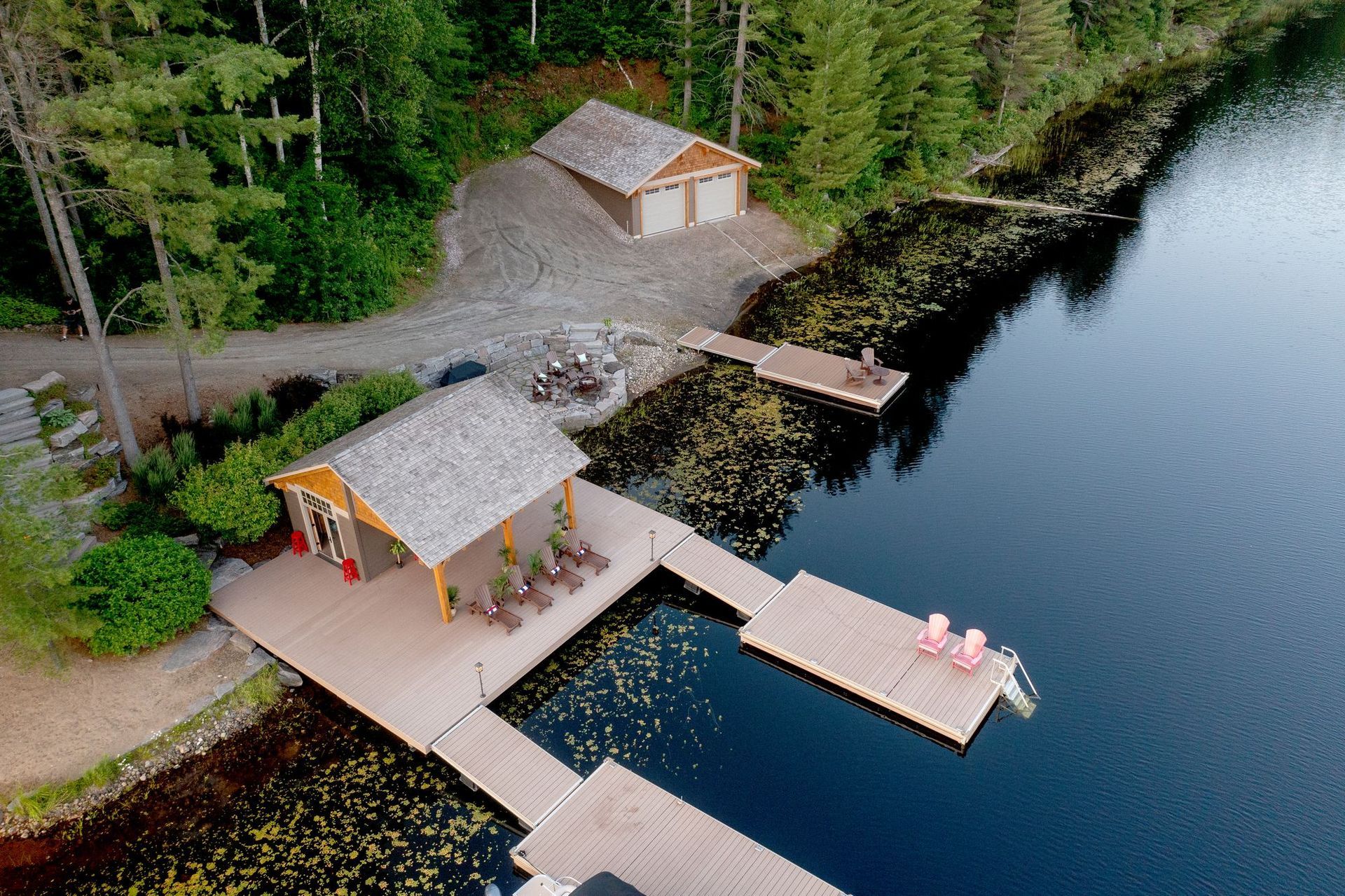 Aerial view of a lakeside cabin with docks, a small boathouse, and forested shoreline