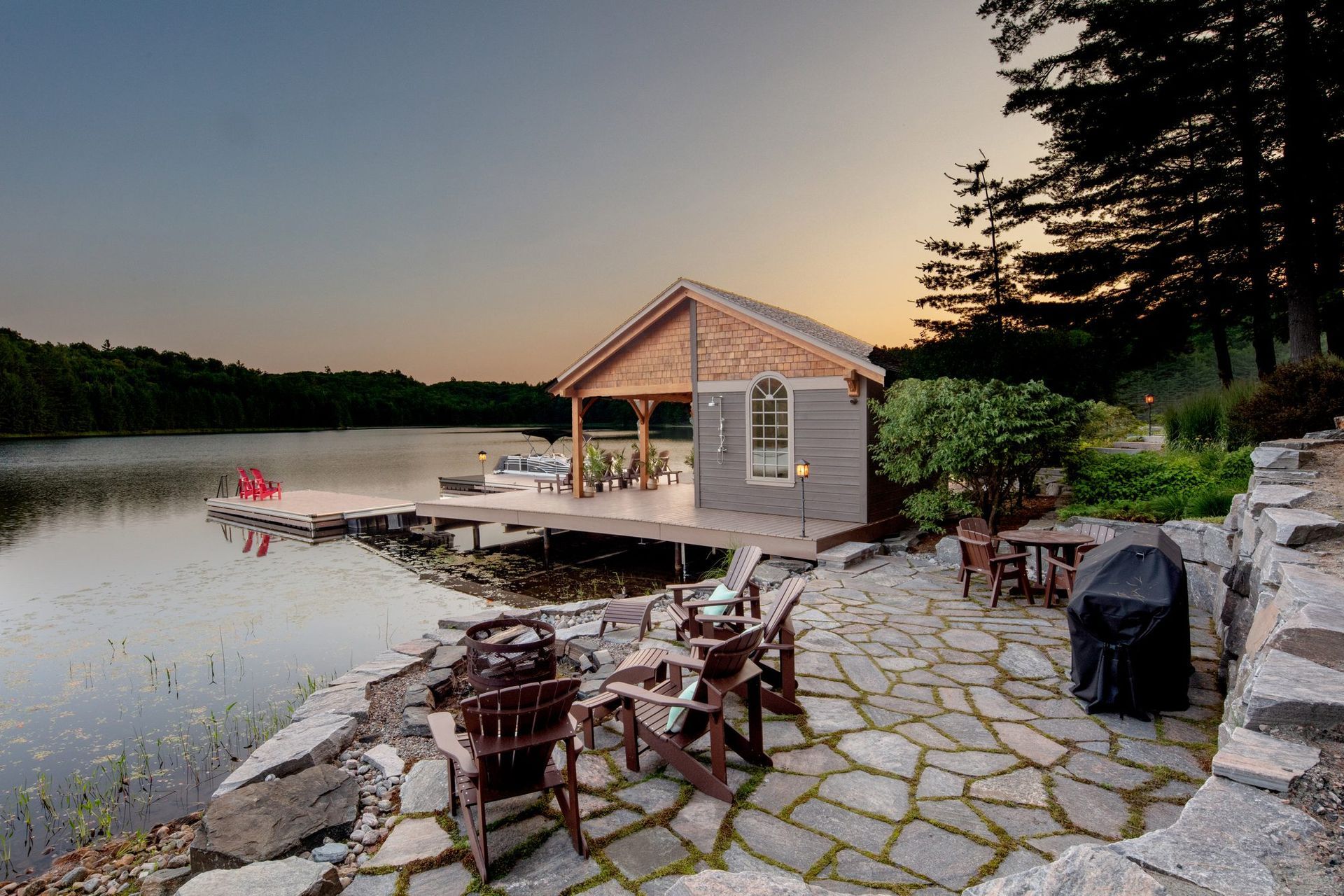 Lakeside cabin with dock and patio chairs at sunset, beside calm water and trees