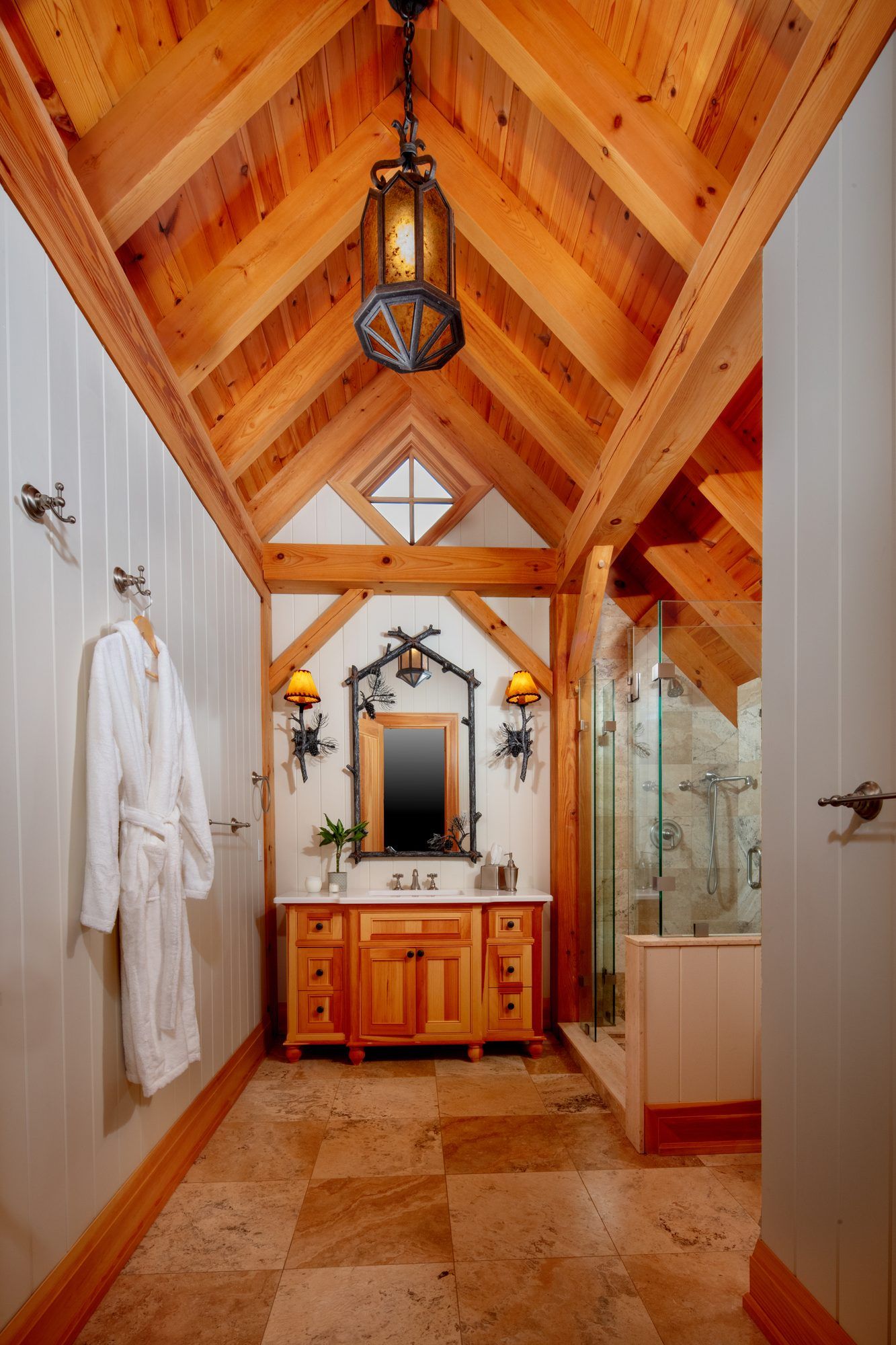 Rustic bathroom with wood-beamed ceiling, vanity, shower, and stone floor in warm tones
