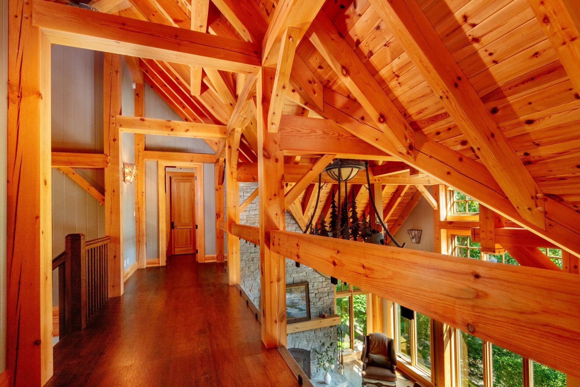 Wooden loft hallway with exposed beams, warm lighting, and windows overlooking greenery