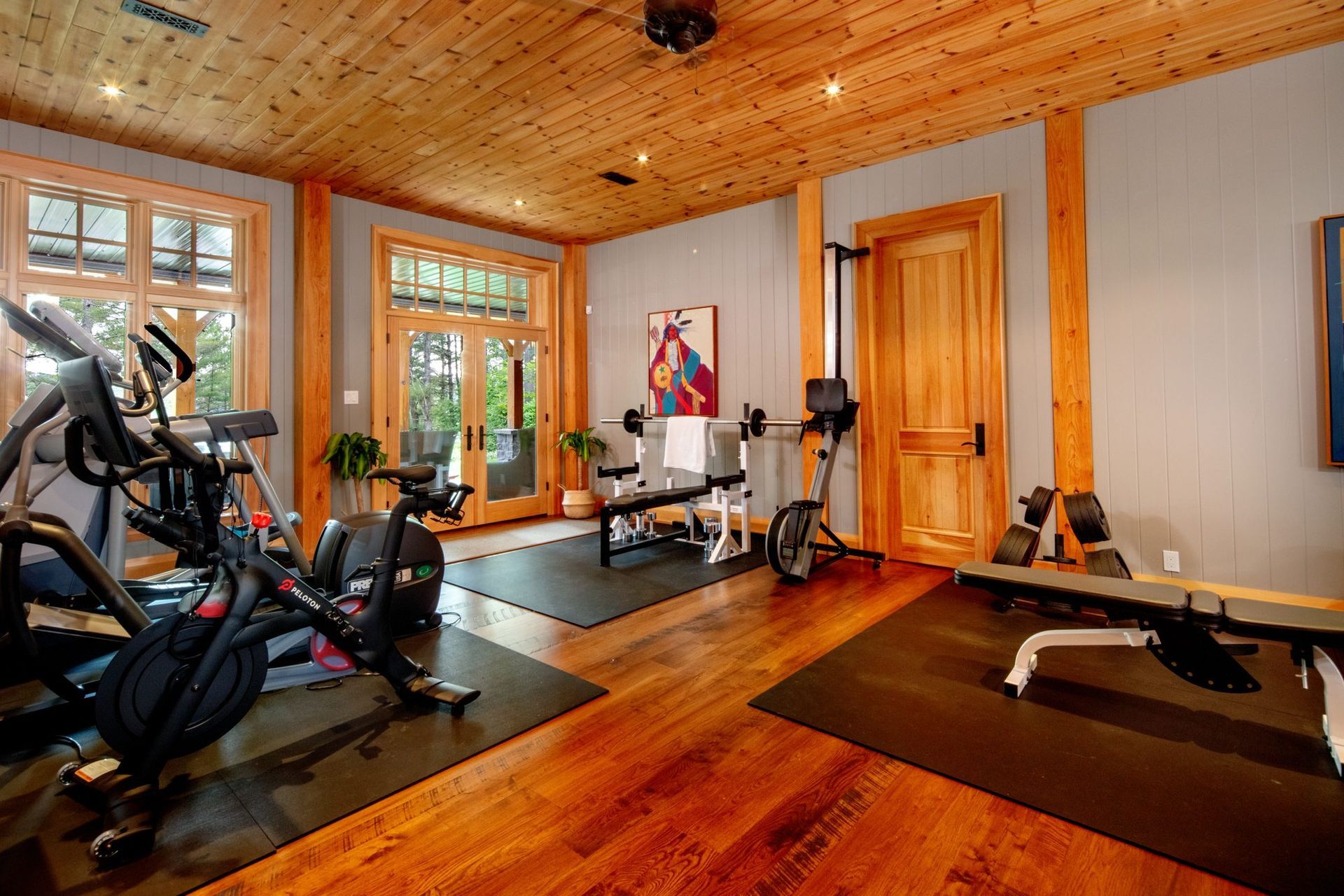 Home gym with exercise equipment, wood floors and ceiling, and large windows letting in natural light