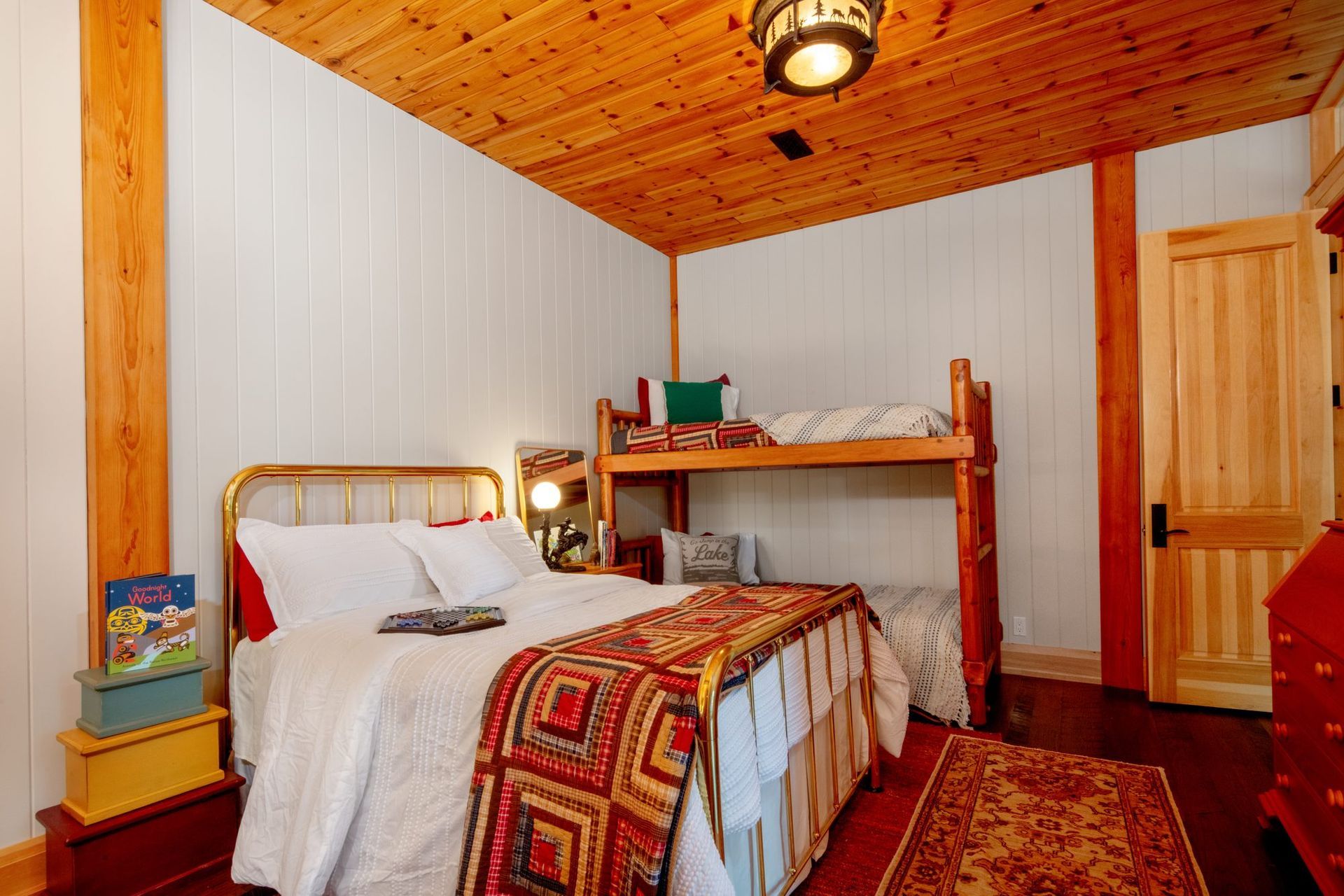 Cozy bedroom with wooden ceiling, twin bed, bunk bed, and red patterned rug