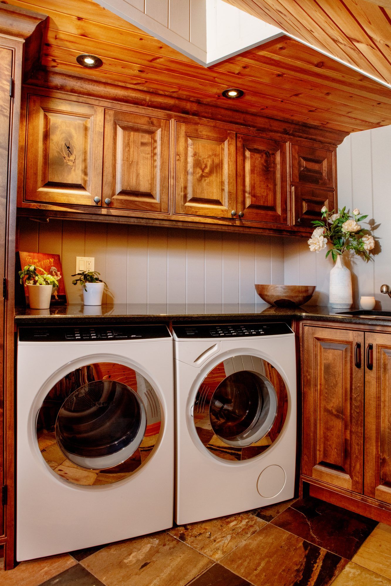 Wooden laundry room with front-loading washer and dryer beneath cabinets and a black countertop