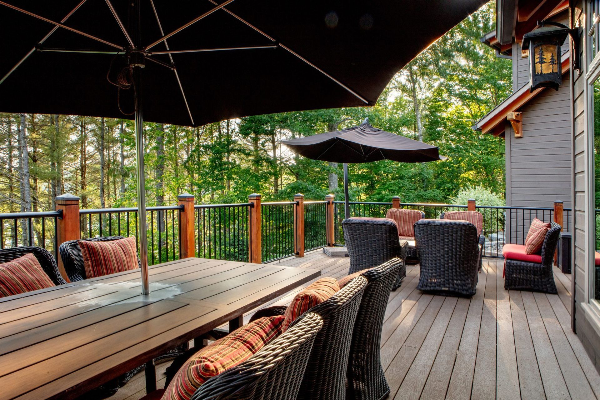 Wooden deck with wicker seating, long table, umbrellas, and forest view