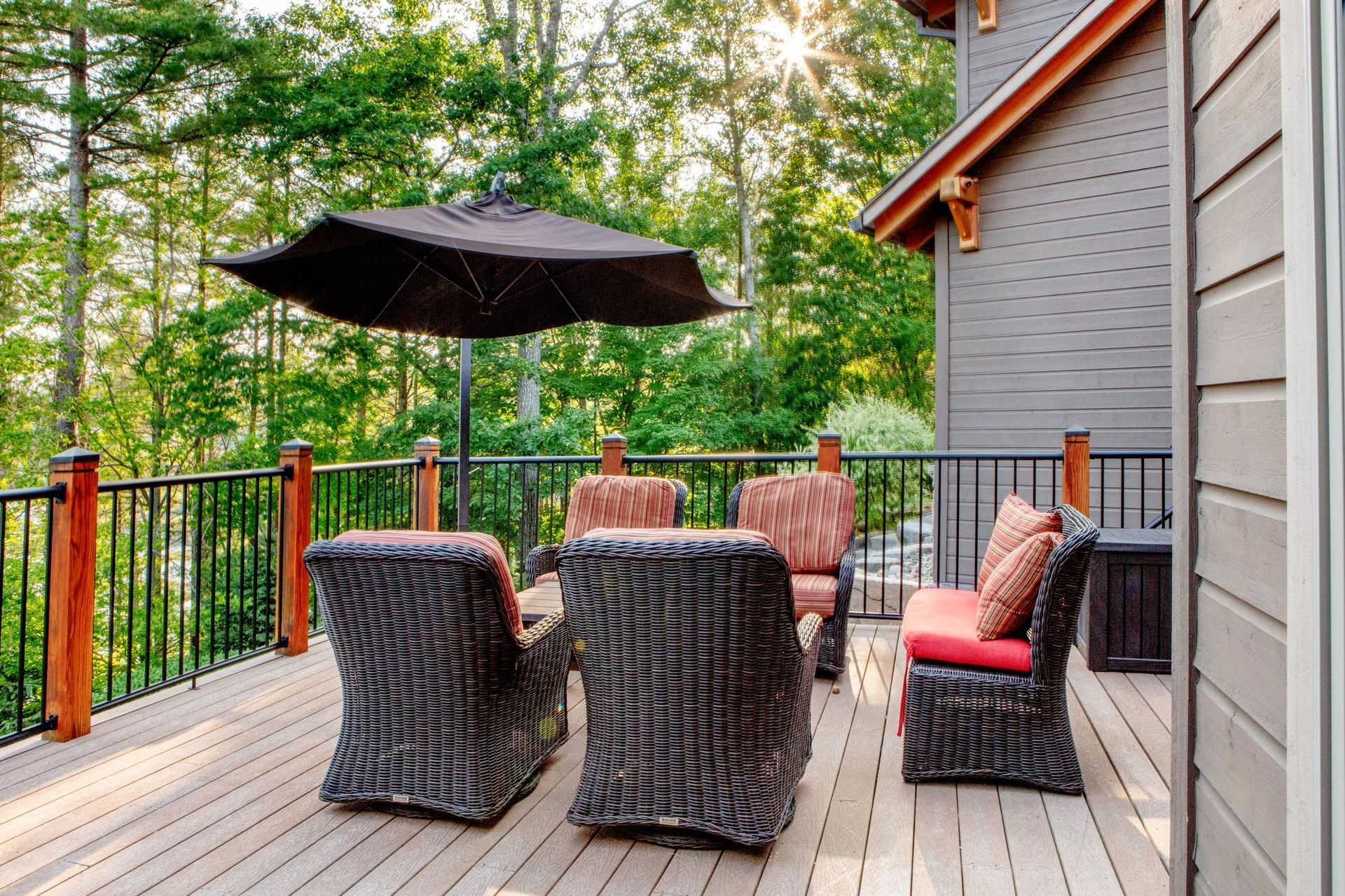 Wooden deck with wicker chairs, black umbrella, and forest view beside a house
