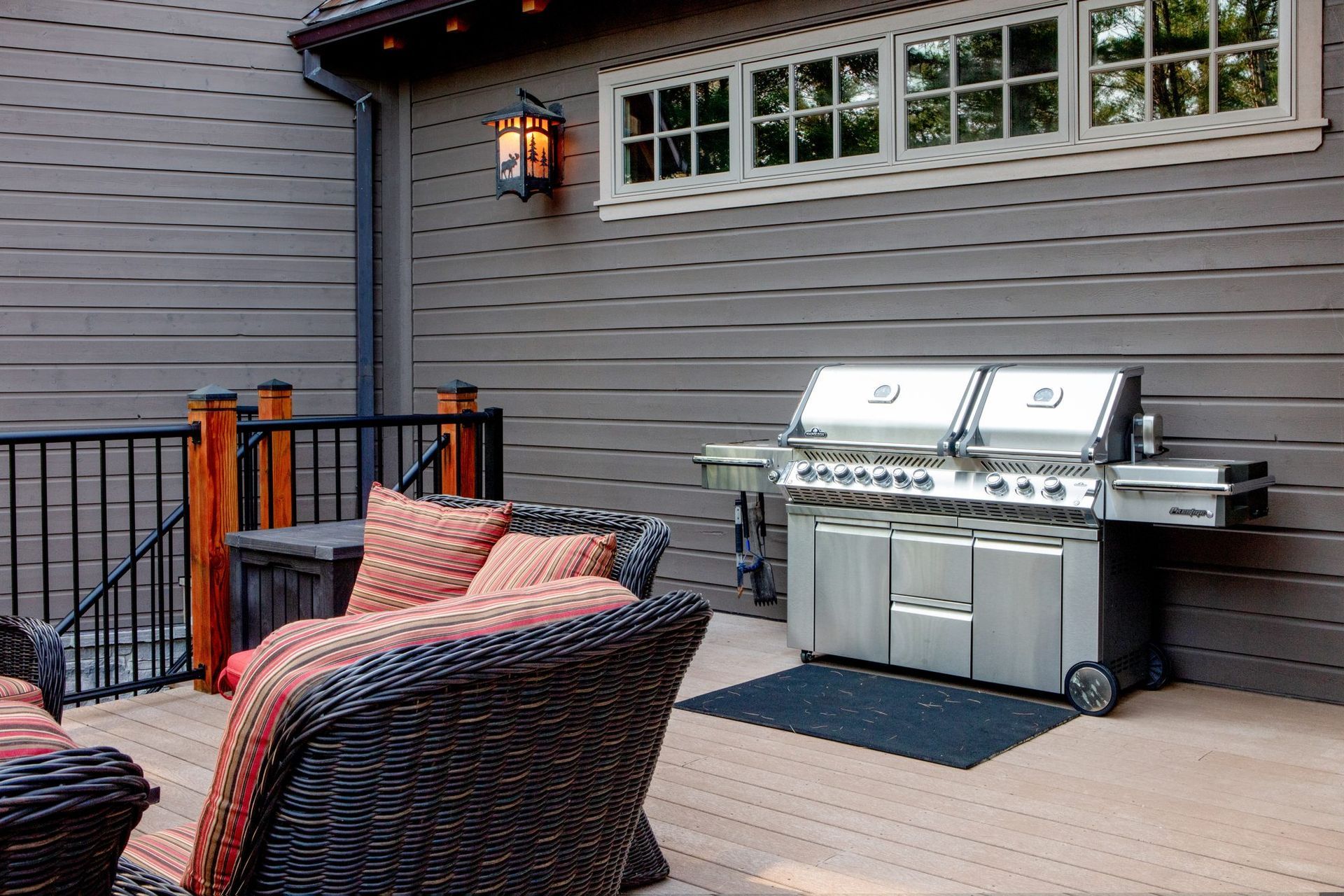 Outdoor patio with wicker chairs and a stainless steel grill beside a gray house wall