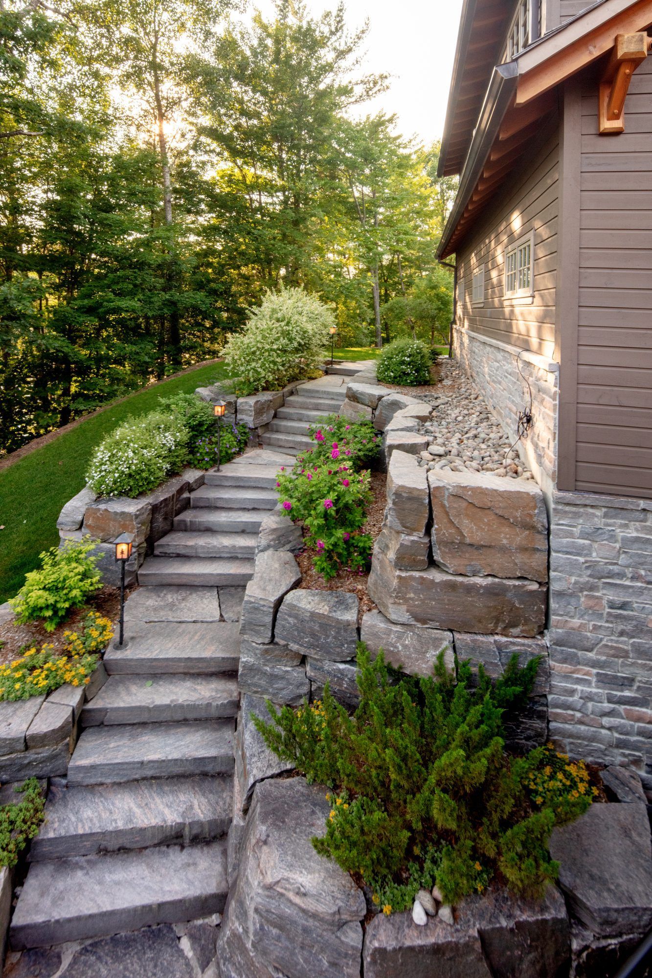 Stone steps beside a house climb a landscaped hillside with shrubs and trees