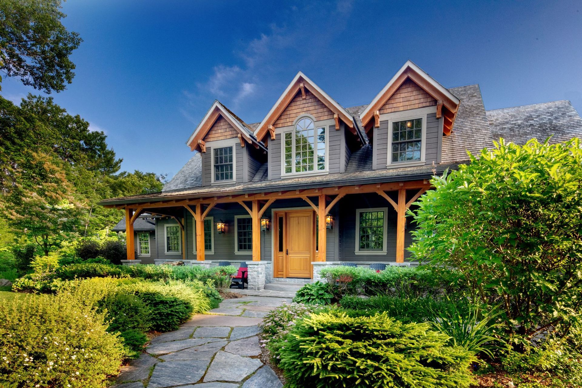 Charming stone cottage with gabled dormers, a front porch, and a garden path surrounded by lush greenery.