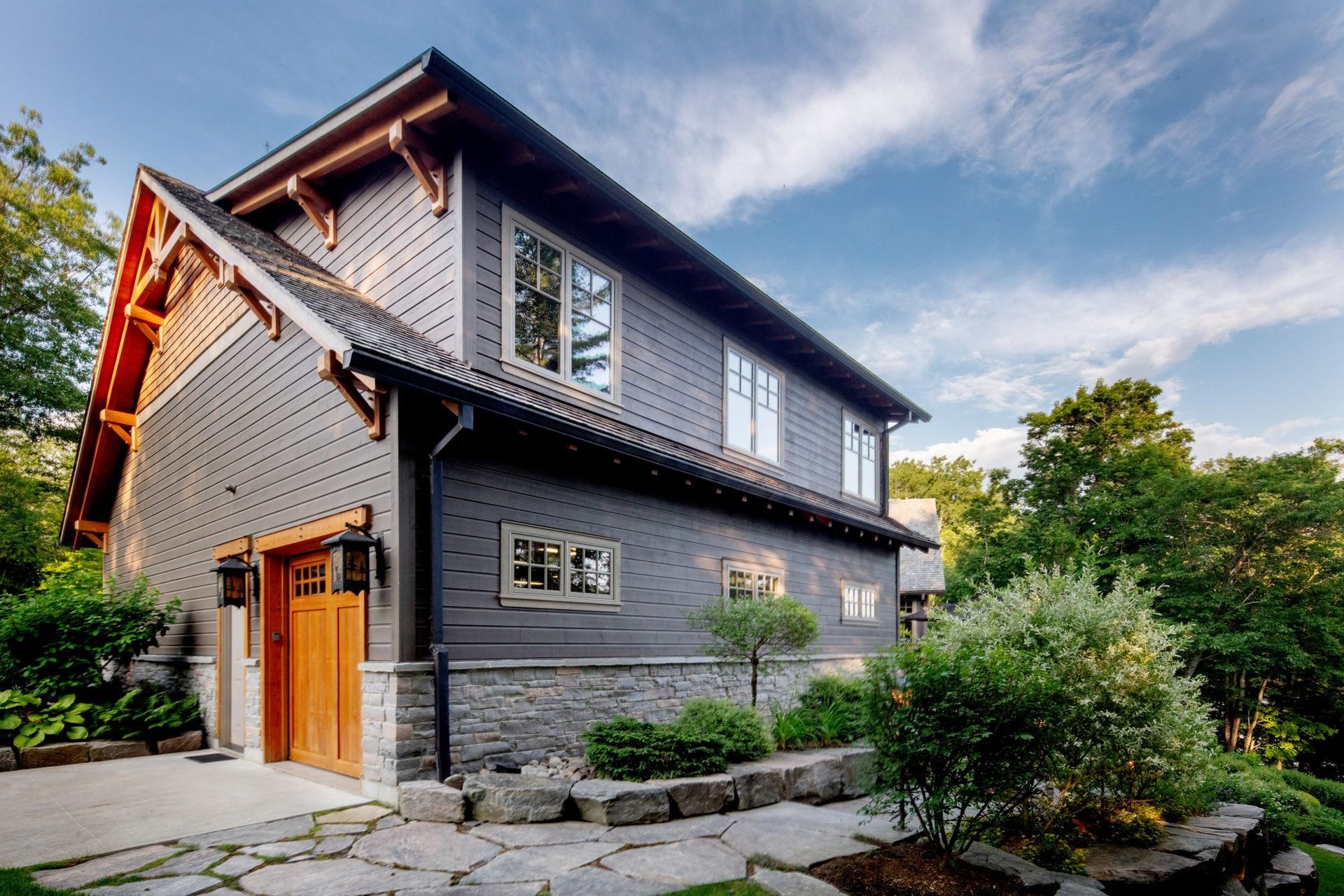 Gray brick house with wooden accents and stone garden path under a blue sky