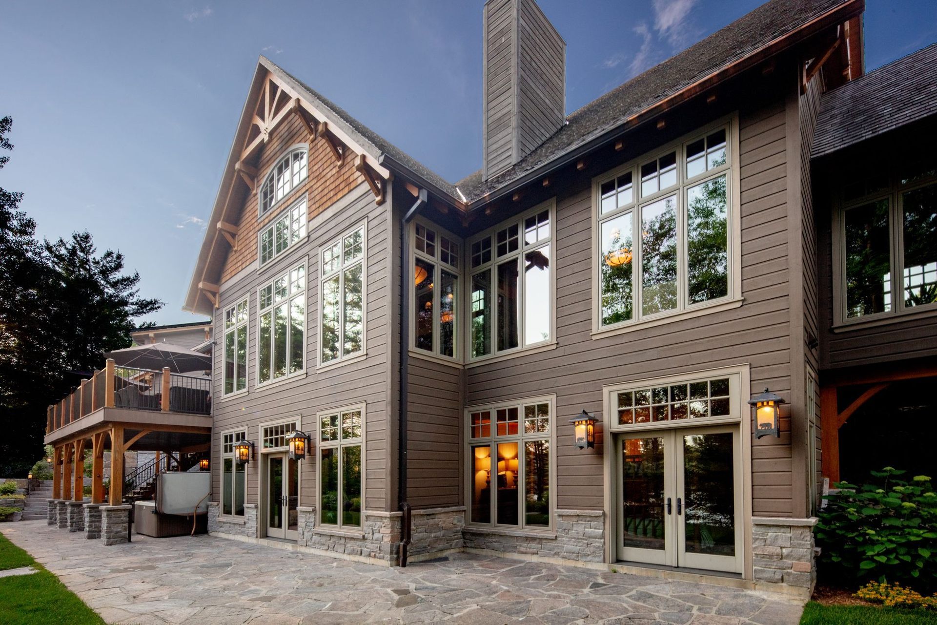 Large brick house with tall windows, stone patio, and a covered entrance at dusk